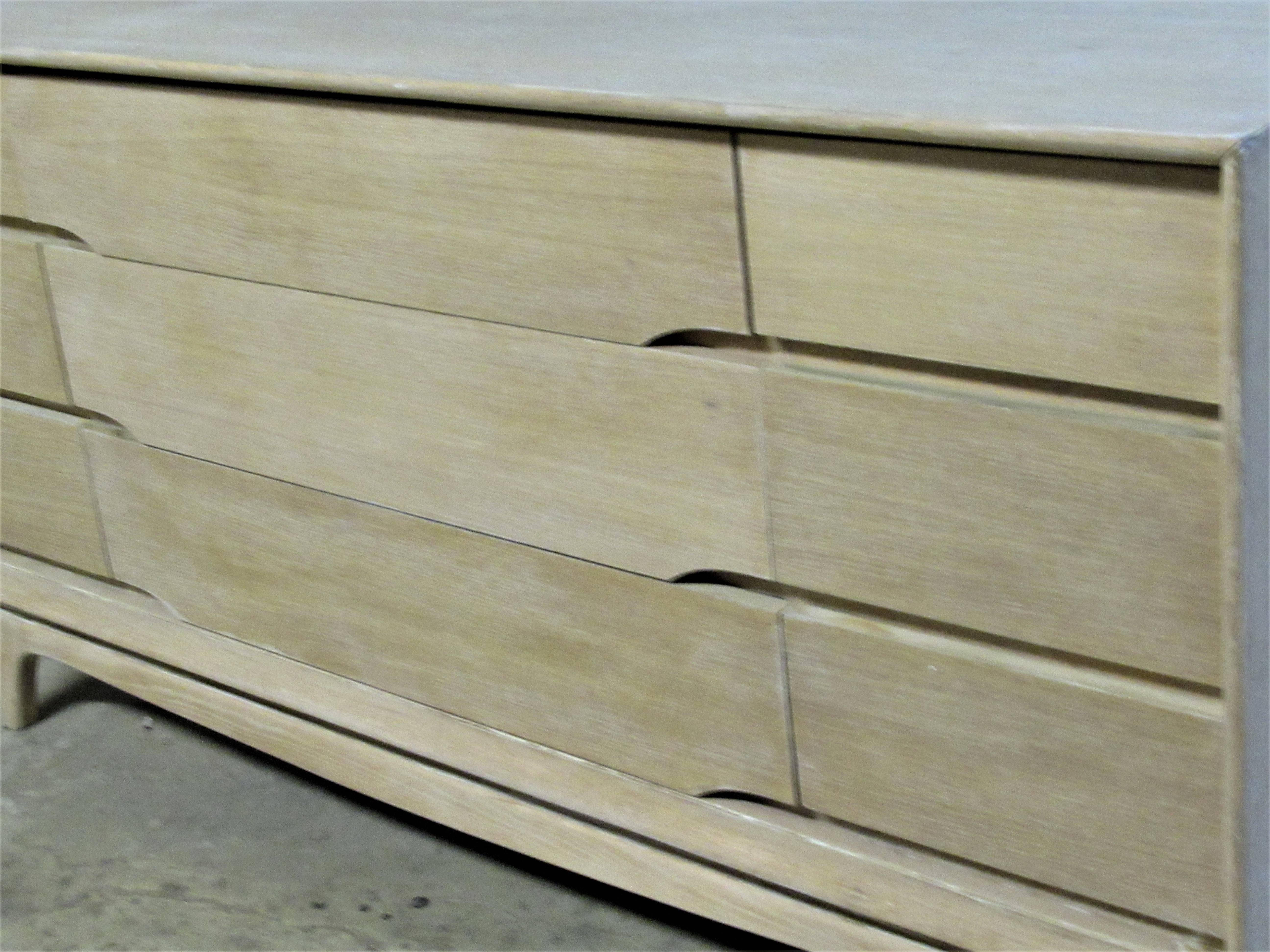A Mid-Century Modernist nine-drawer credenza dresser (three long central drawers - six short side drawers) with a very sleek sculptural form. The wood has been stripped, bleached and cerused to a very pale parchment color. See all pictures.