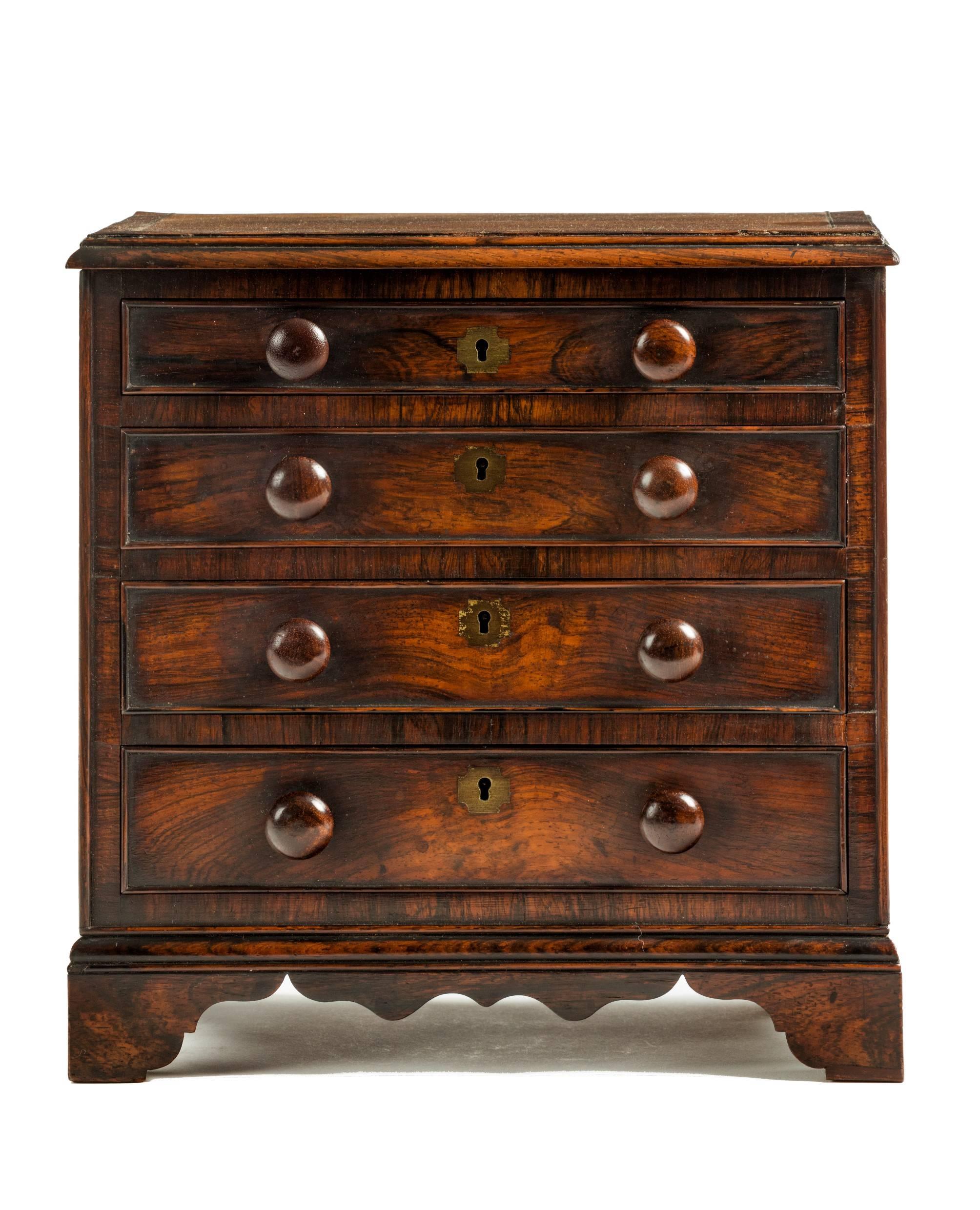 A fine example of a miniature chest of drawers. An apprentice piece or tradesman's sample. Veneered in rosewood with brass inlay. Four long graduated drawers, original locks, handles and bracket feet. The whole is free-standing with veneered sides