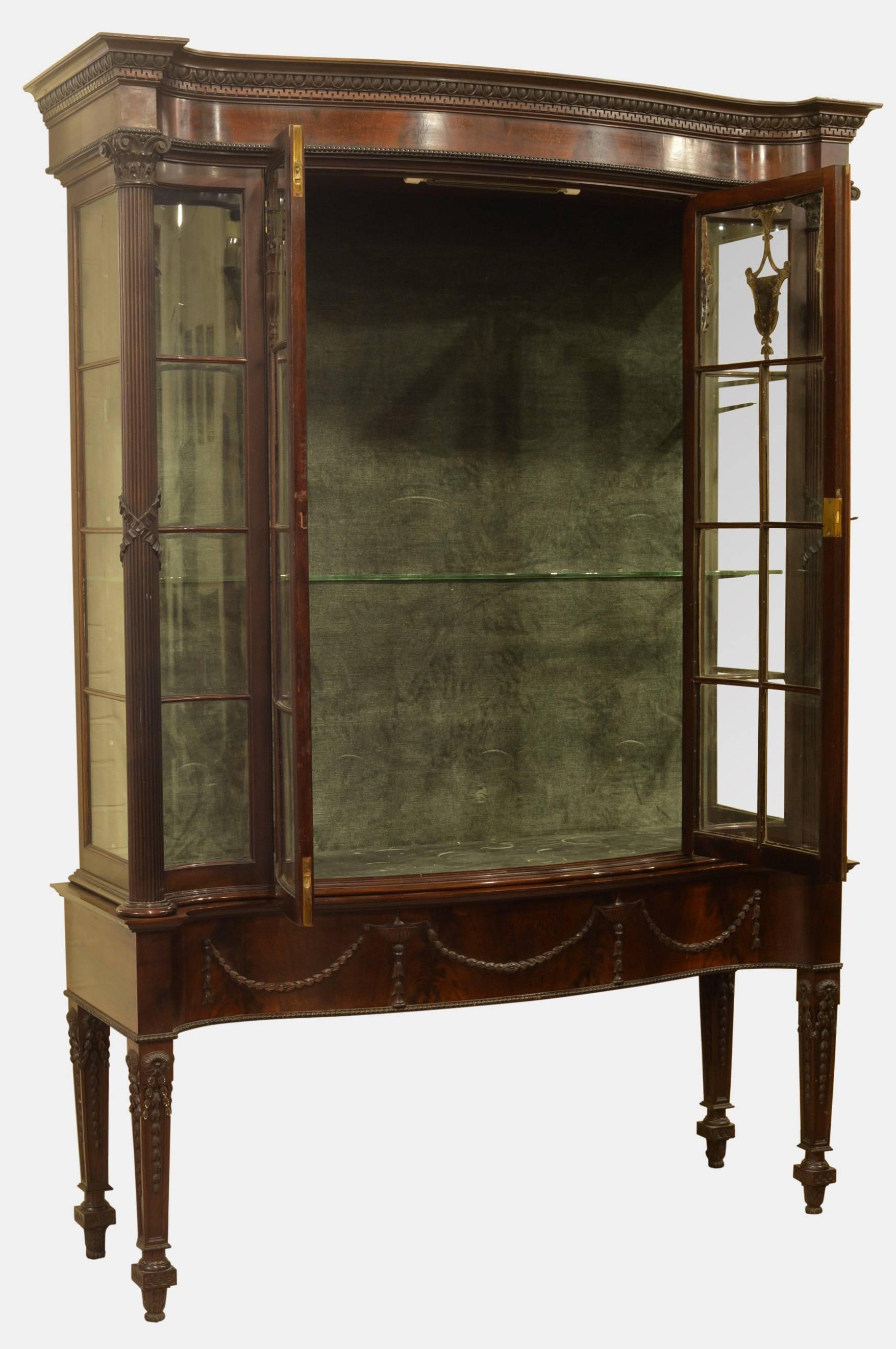 A fine mahogany serpentine fronted display cabinet with astragal glazed doors and ends decorated with classical urns and harebell swags.
The base unsuited standing on square tapering legs also decorated with harebell swags. the cornice with egg and