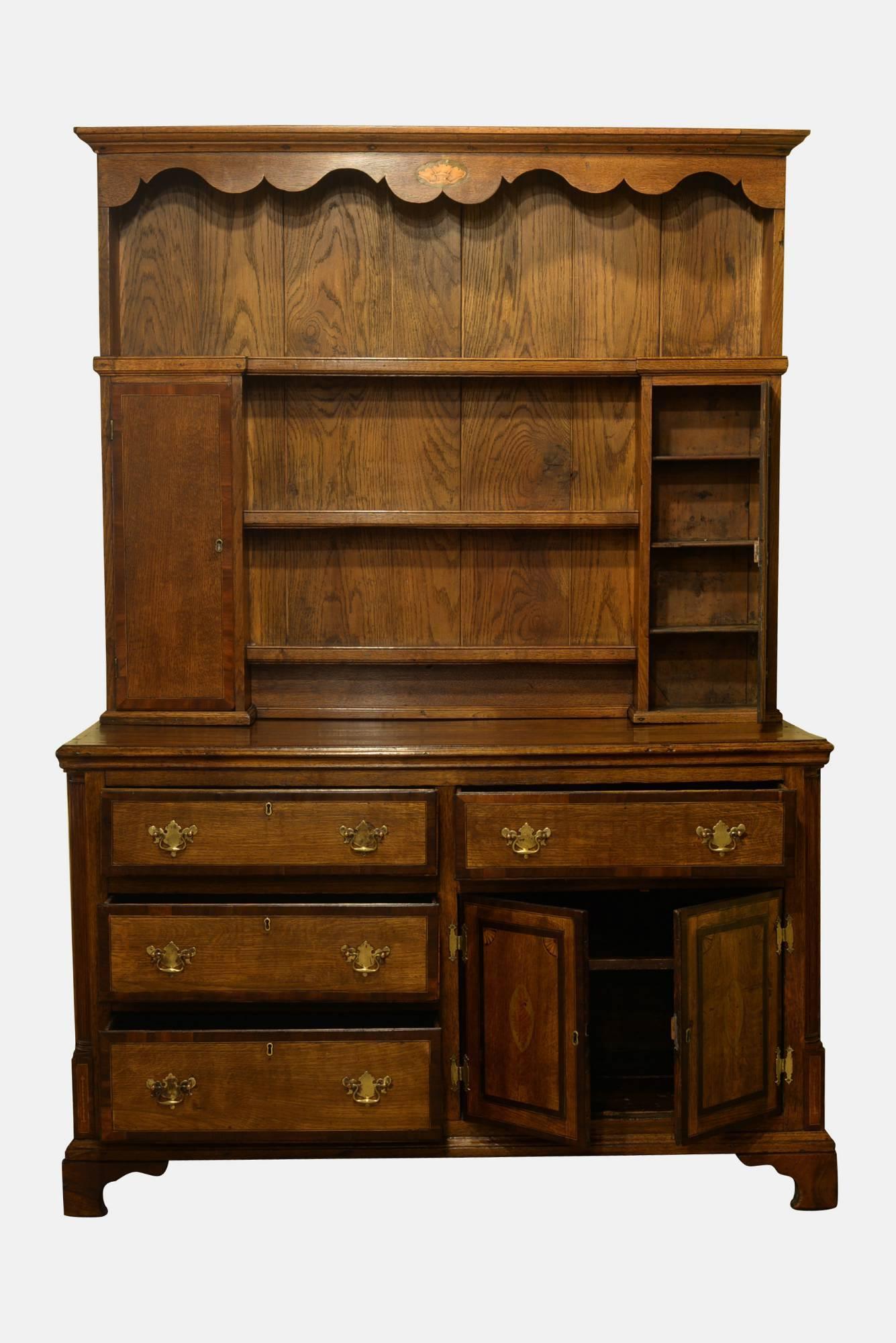 Early 19th century oak high dresser, the plate rack has a moulded cornice with central shell inlay above three open shelves flanked by two cupboard doors. The base with rectangular top above an arrangement of four drawers and two doors. The whole
