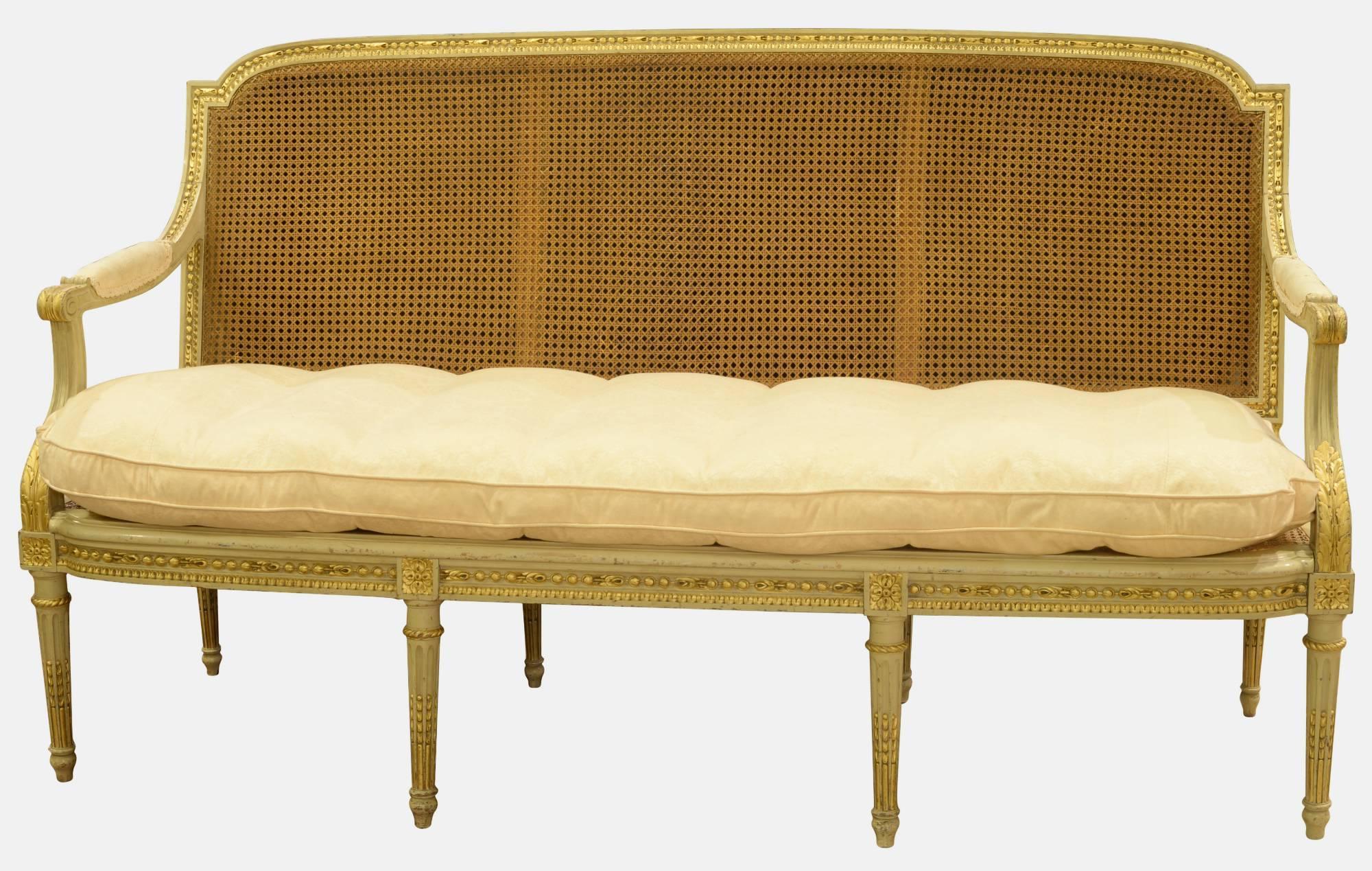 French Louis XVI style painted and gilded sofa on turned, fluted legs with caned seat and back. With squab cushion, circa 1900.