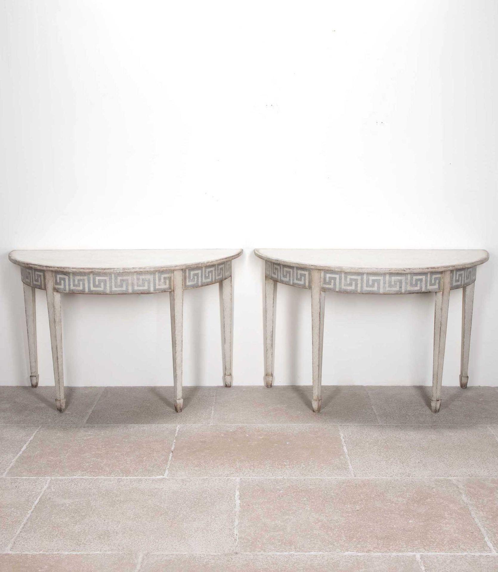 A charming pair of late 19th Century Swedish demi-lune tables, later painted in soft, neutral tones. 
Featuring elegant tapered legs and classic painted Greek Key detailing along the apron, these tables blend timeless neoclassical influence with