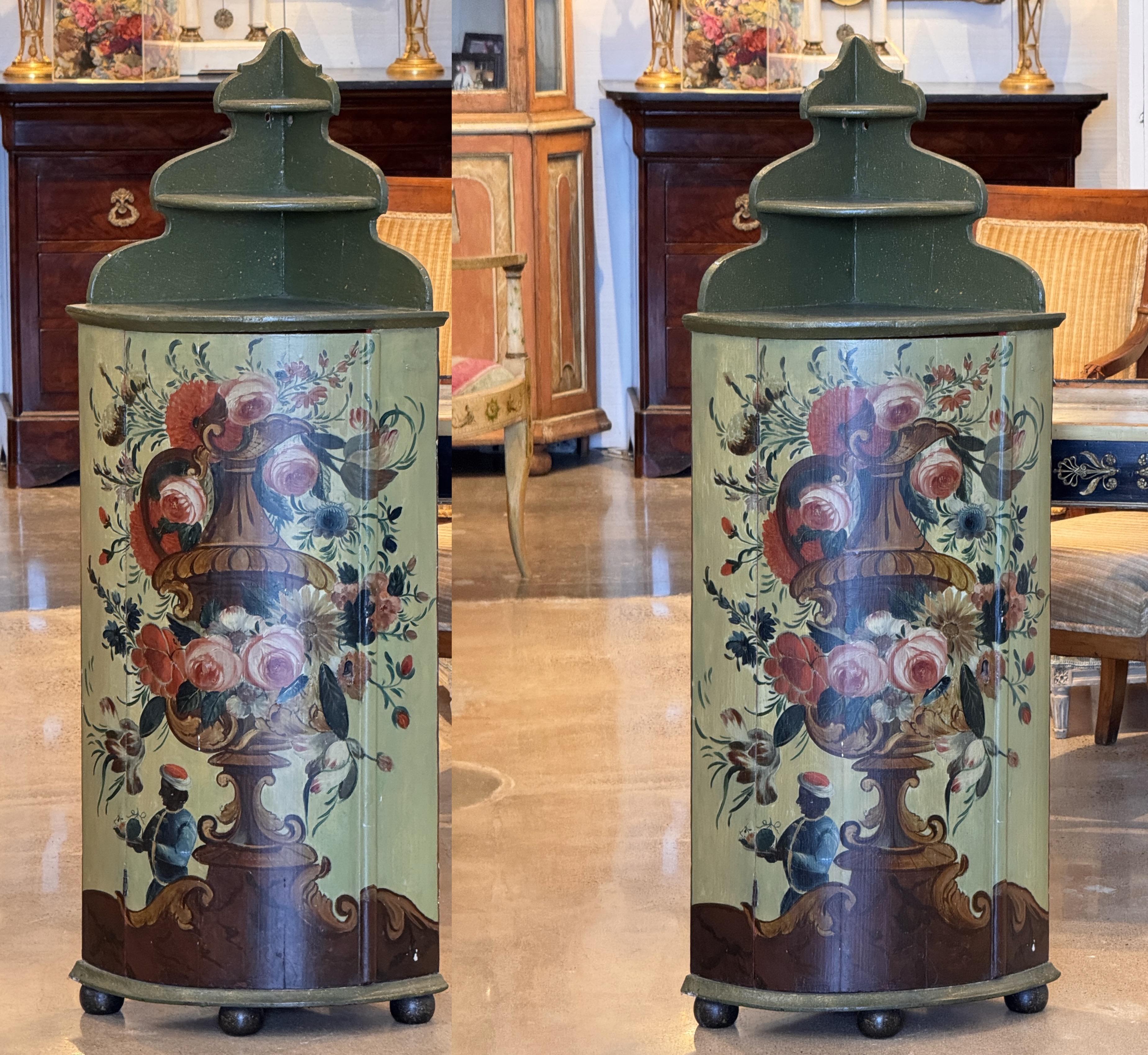 Zwei bemalte Eckschränke aus dem 19. Jahrhundert mit geformten Aufsätzen, gedrechselten Füßen und Innenregalen. Die Fronten sind mit großen Blumenurnen und stilisierten Figuren in leuchtenden Farbtönen verziert, während die Innenräume tiefrot bemalt