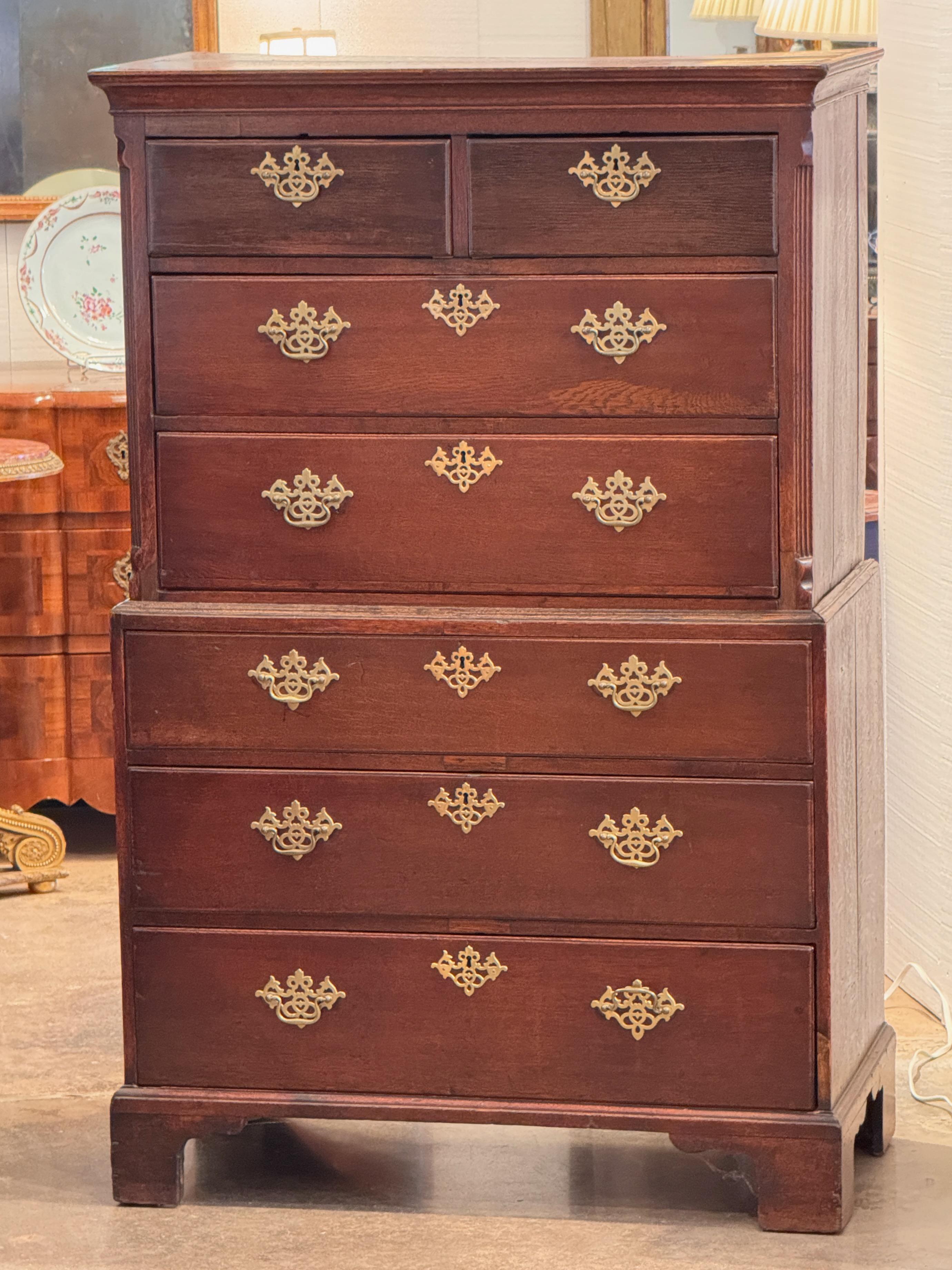 English chest-on-chest in oak, late 18th century, with molded cornice, fluted corners, and brass escutcheons and pulls. The upper section features two short drawers over three long, set above a lower chest of three full drawers. Traditional bracket