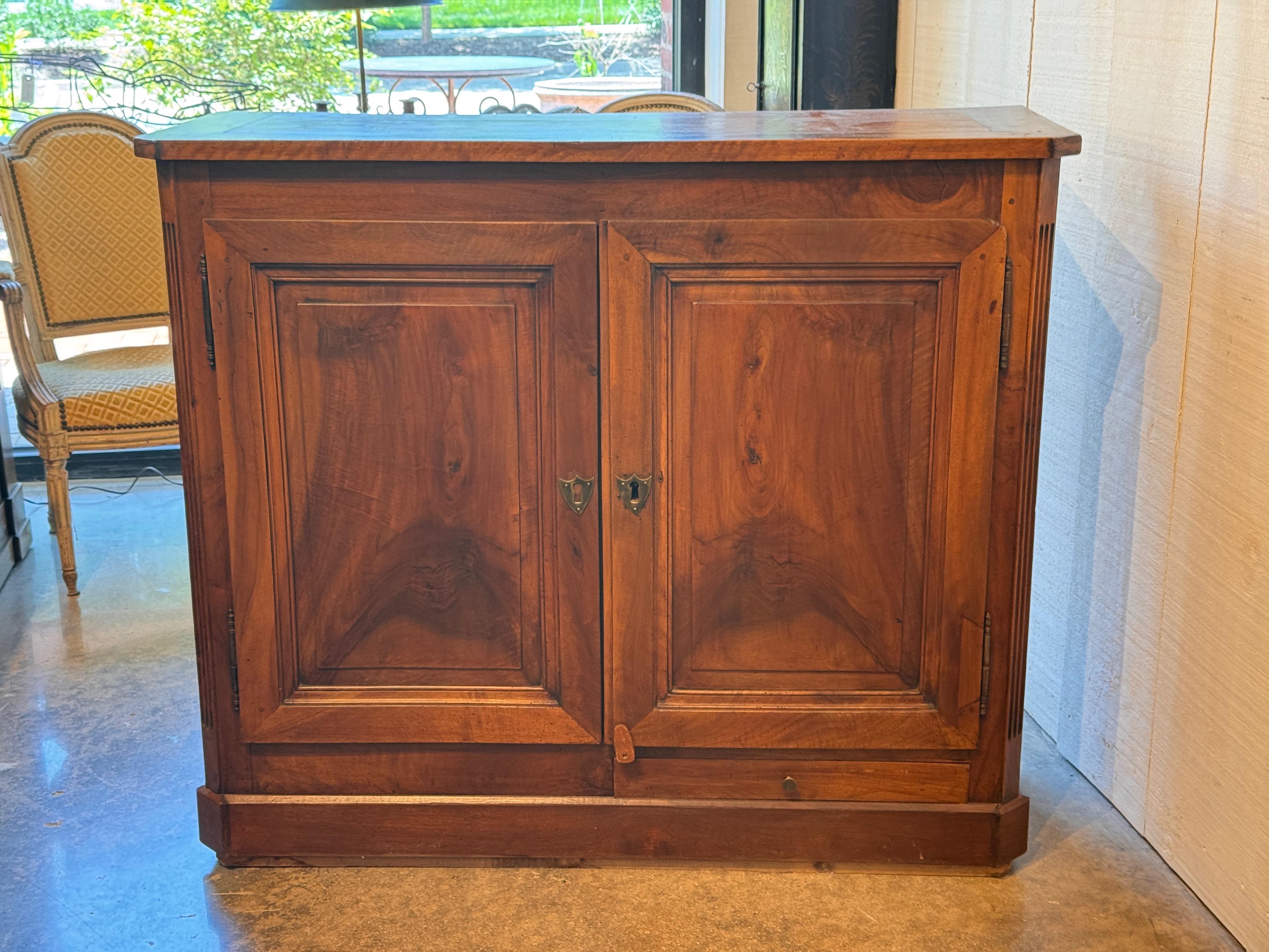 Mid-19th century French Louis Philippe buffet in solid walnut, featuring paneled doors with molded edges and subtle grain patterning. The case rests on a shaped plinth base and includes a hidden lower drawer. Interior shelving provides practical