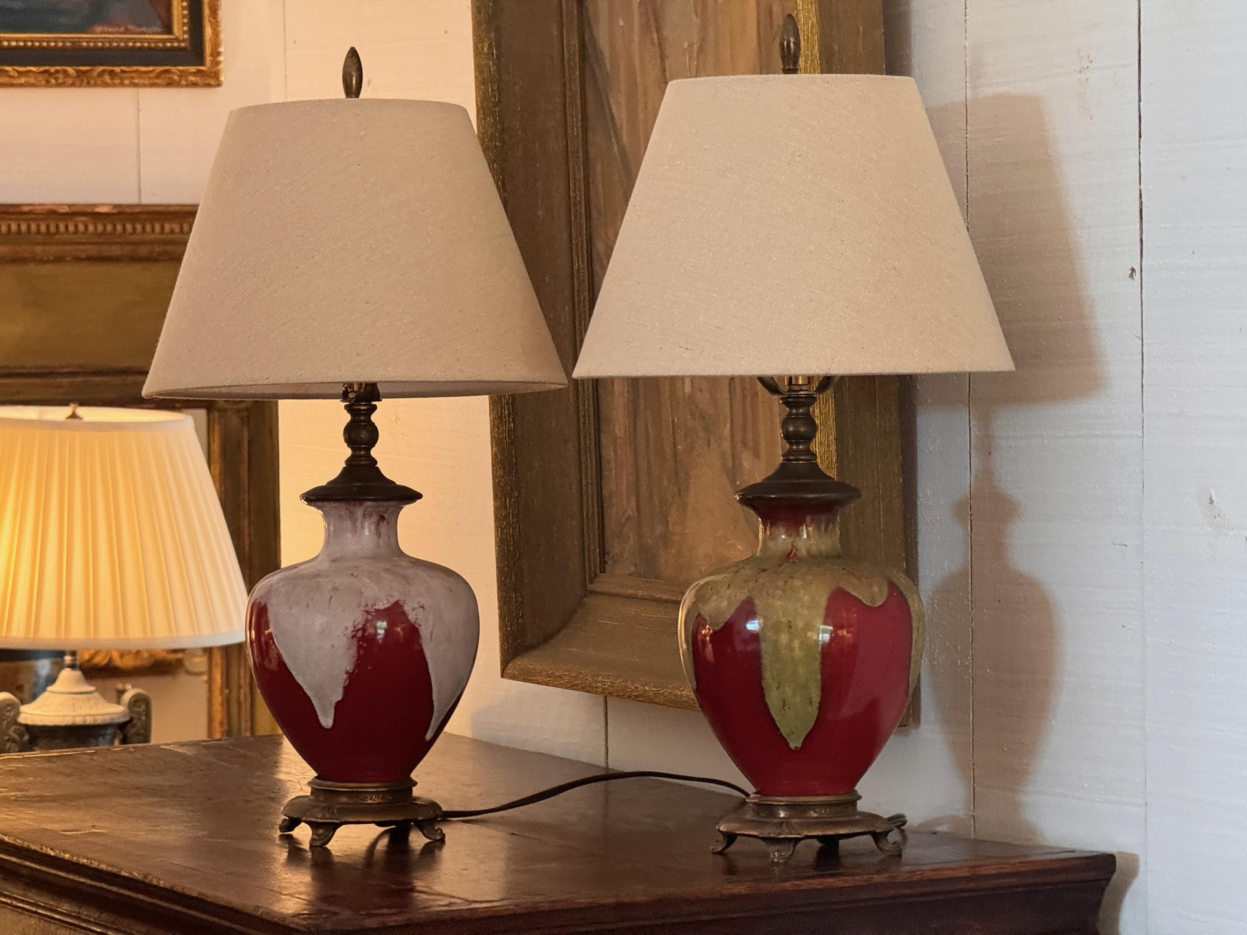 Pair of table lamps converted from Sang de Boeuf glazed vases with rich oxblood red and dramatic drip glaze. Each sits on an ornate bronze base with paw feet. The crackled surface and tonal variation highlight the character of the glaze, rooted in