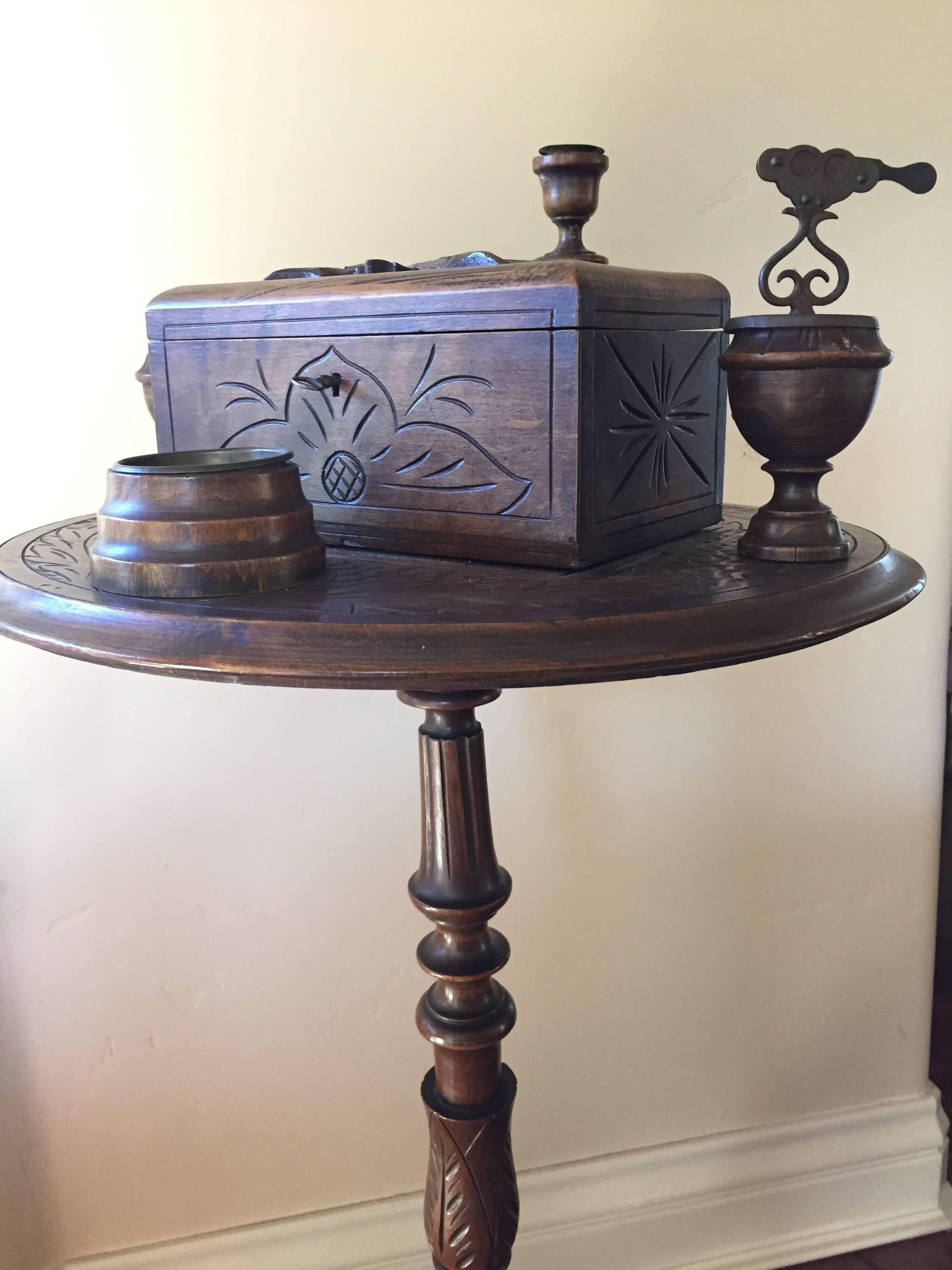 This fantastic Black Forest oak smoking stand is expertly carved and has attained a mellow patina with age, the humidor with original working lock and key surmounted with carved leaves and branches, the cigar and cigarette cutter
present and