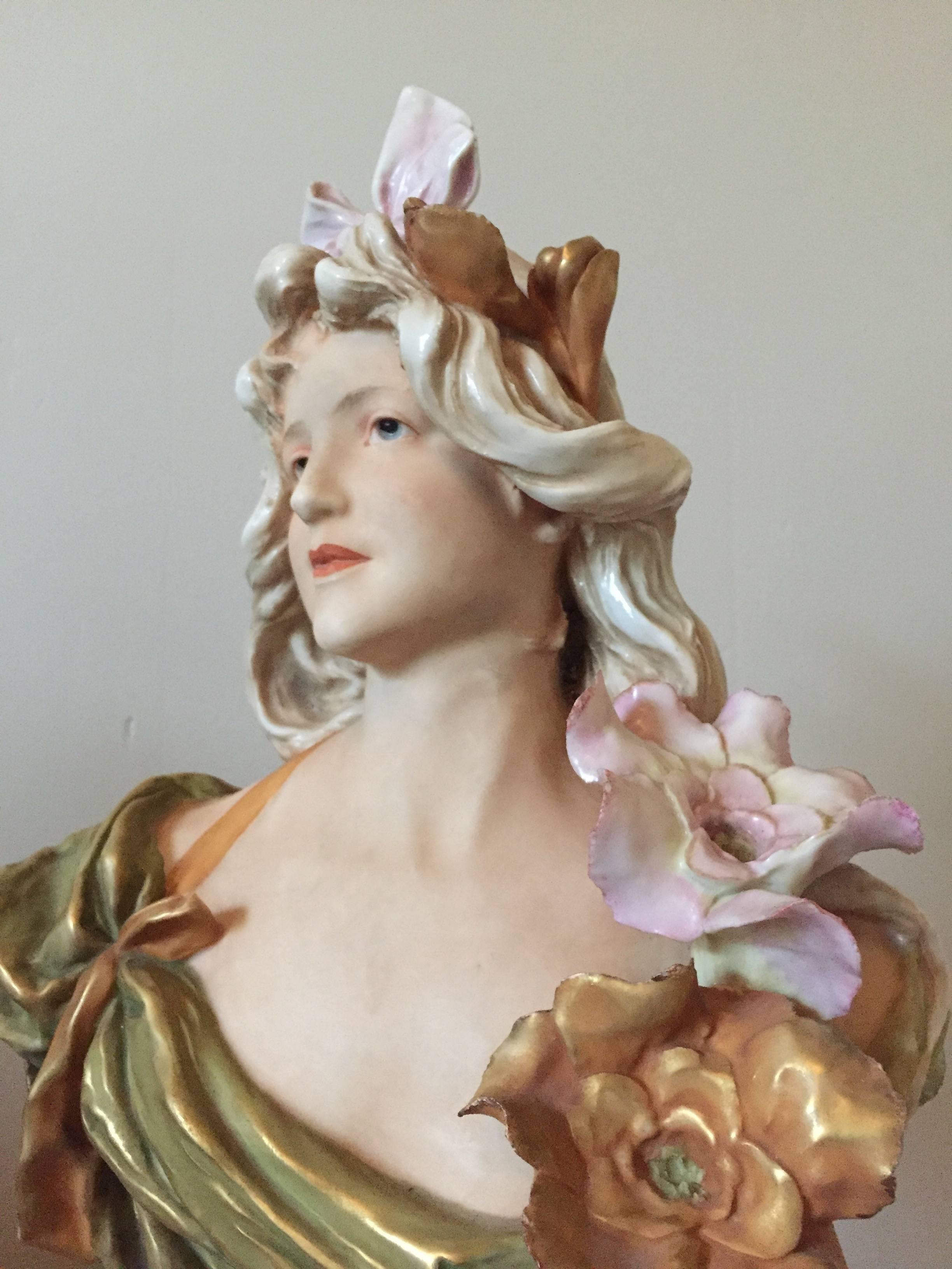 This beautiful Art Nouveau bust by Royal Dux of Austria is a perfect example of the work done by this firm during the period. The bust expertly modeled with exceptional details the applied flowers, the coloration lovely and gilt highlighting to
