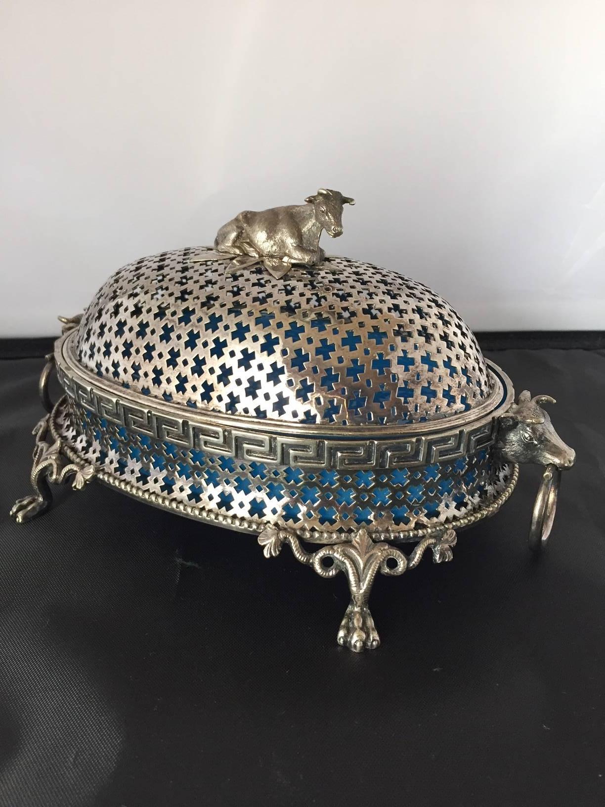 A very rare butter dish, the dome cover pierced and with a reclining cow, the expert artisanship including crisp casting and chasing, and the design fantastic the Greek key, cow heads flanking, and the base supported by paw feet with beautiful open