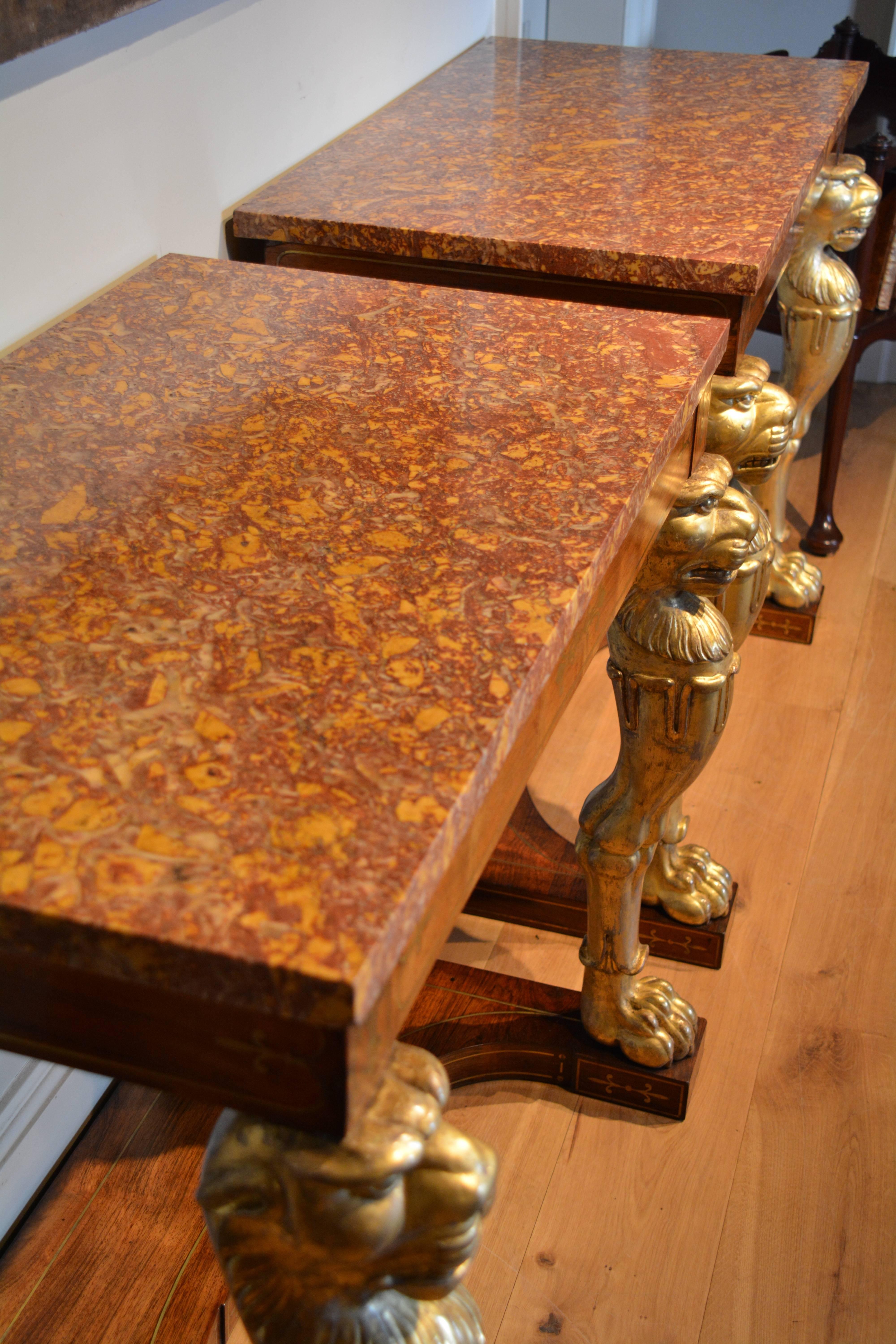 A fine pair of early 19th century brass inlaid rosewood and carved gilt marble-top side tables, the finely figured Spanish Brocatelle marble tops above a rosewood brass inlaid frieze, supported in the front by carved giltwood lion monopodia legs,