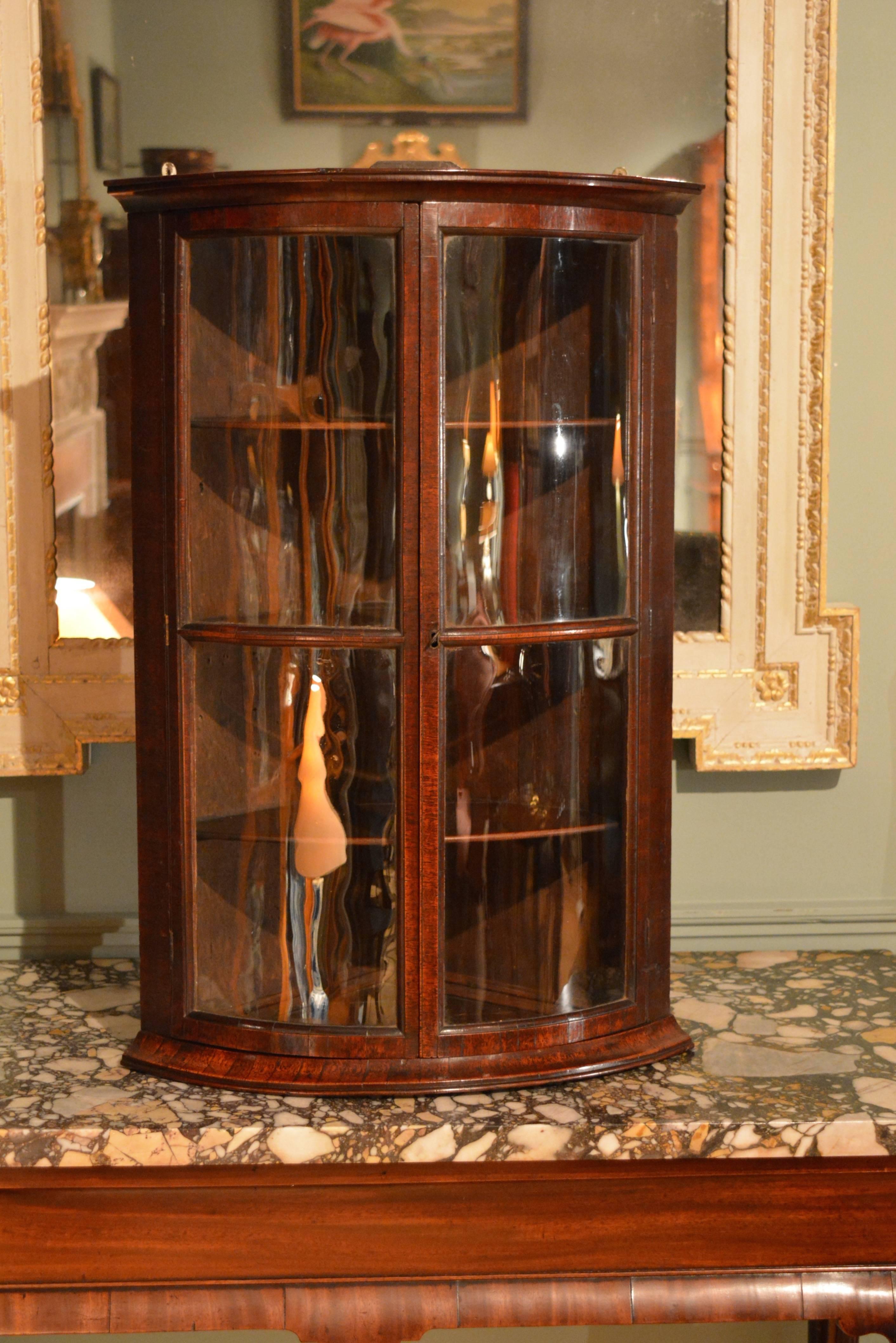 An unusual George II bow fronted, glazed walnut corner cupboard of good colour retaining it's original glass.
