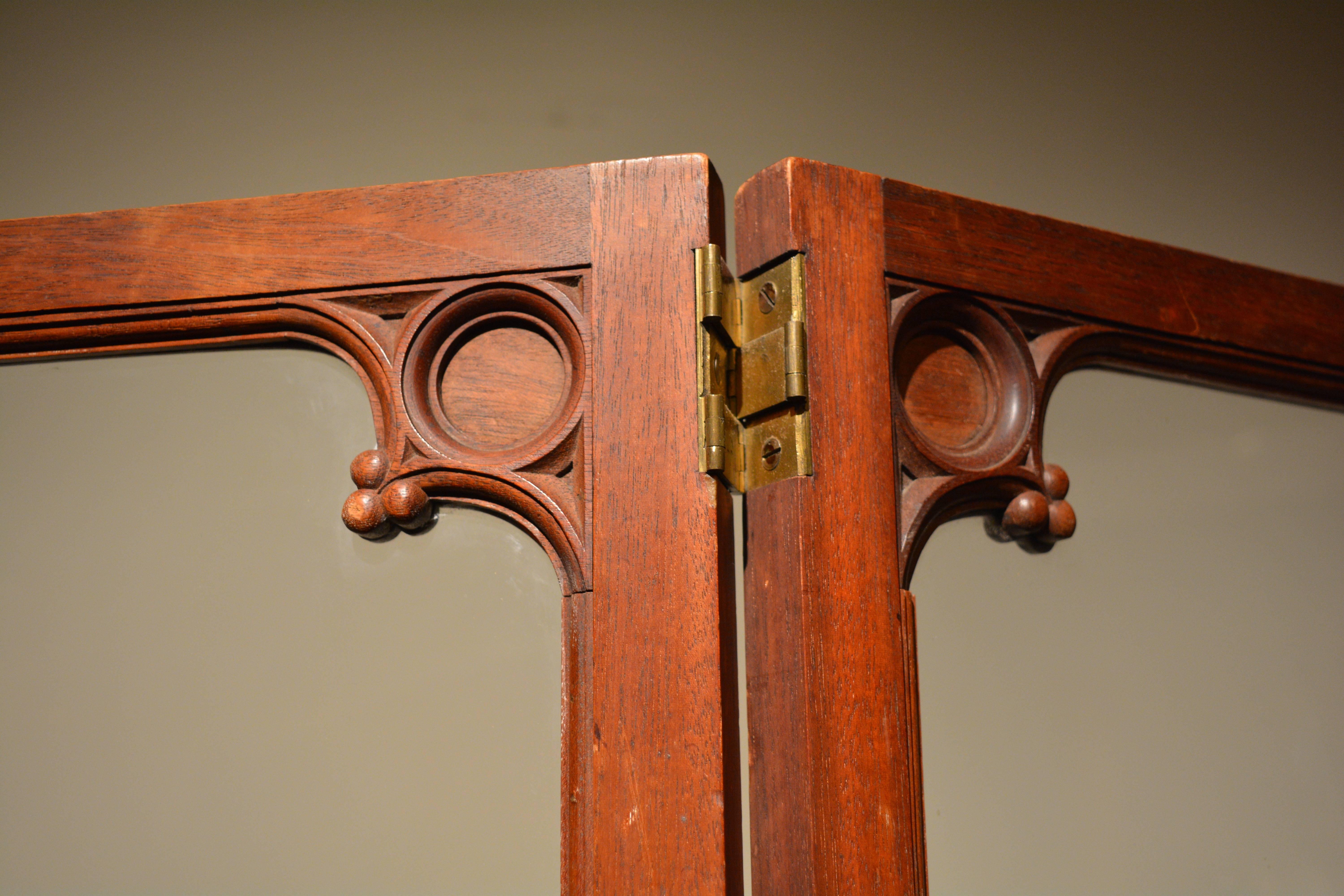 A George IV two-fold mahogany screen, each fold divided into two panels. The upper glazed, the lower filled with green baize, each ornamented by carved re-entrant neo-Gothic corner decoration, English, circa 1825.