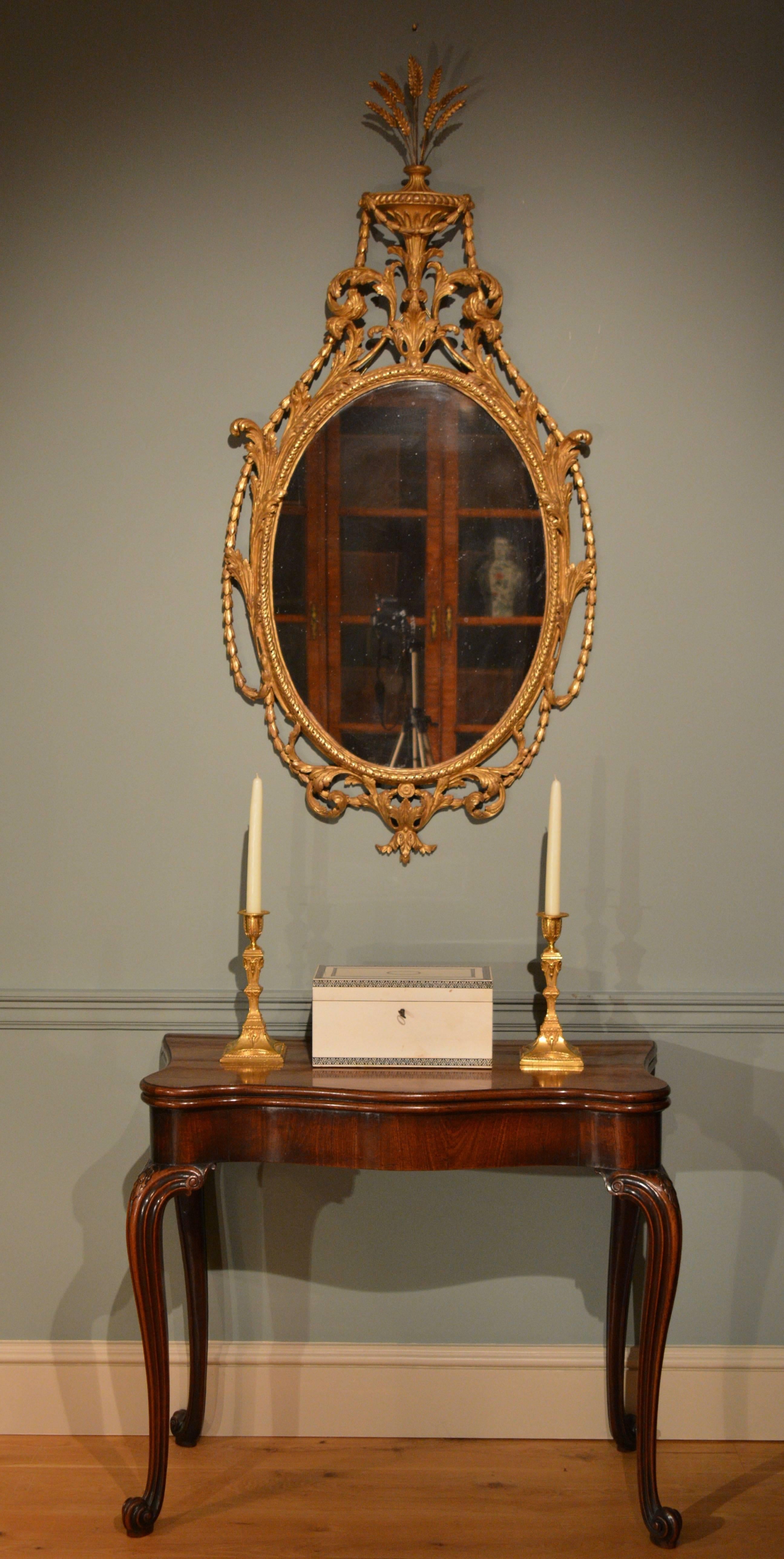 A fine carved wood neoclassical mirror, the oval plate surmounted by an urn sprouting corn below which hand-carved wood swags that surround the frame, interspersed with scrolling acanthus.