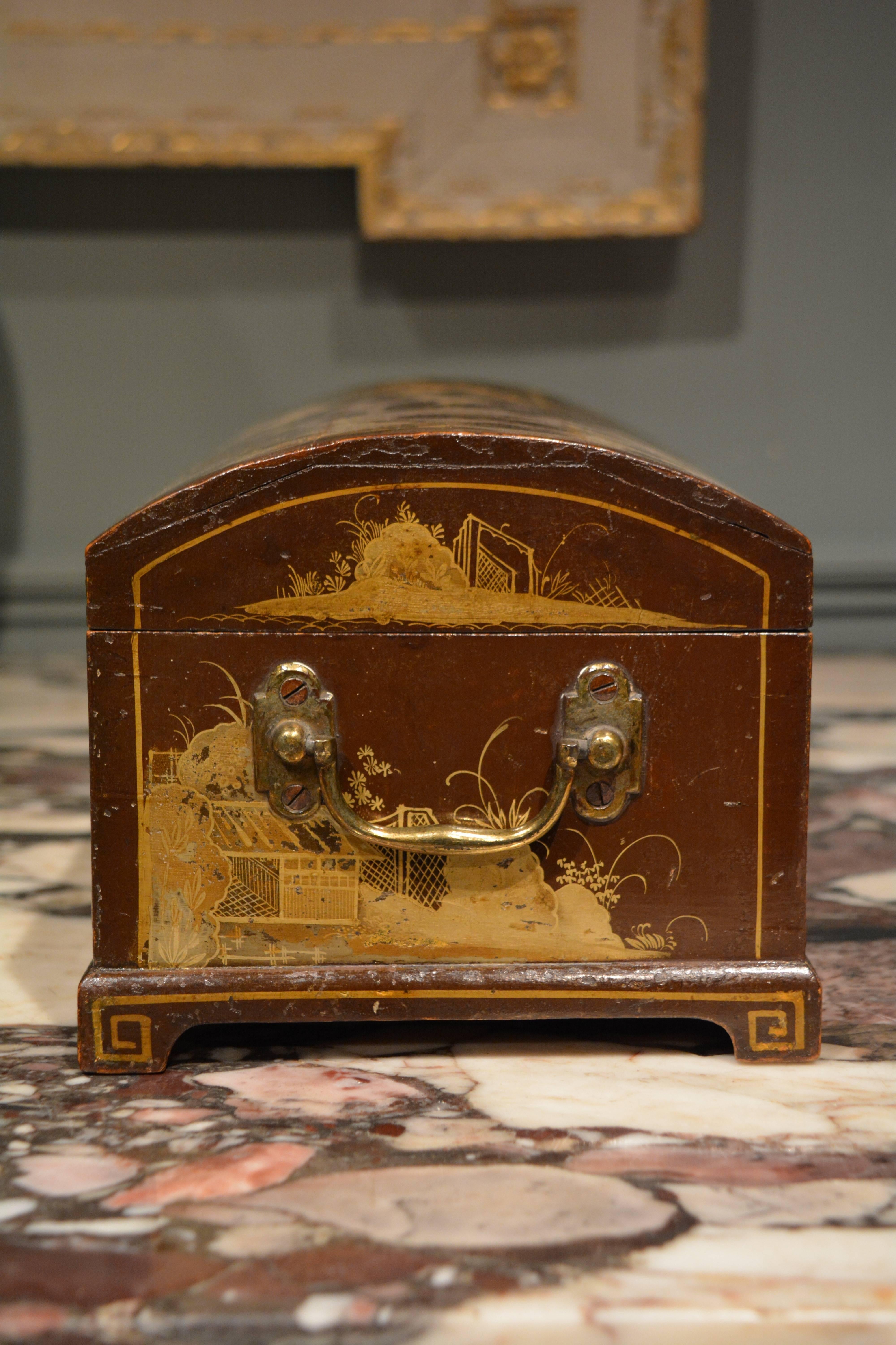 An early japanned dome top casket, the brown ground finely decorated in gilt with oriental scenes, standing on bracket feet and having a finely engraved escutcheon with carrying handles to the end, English, circa 1720.