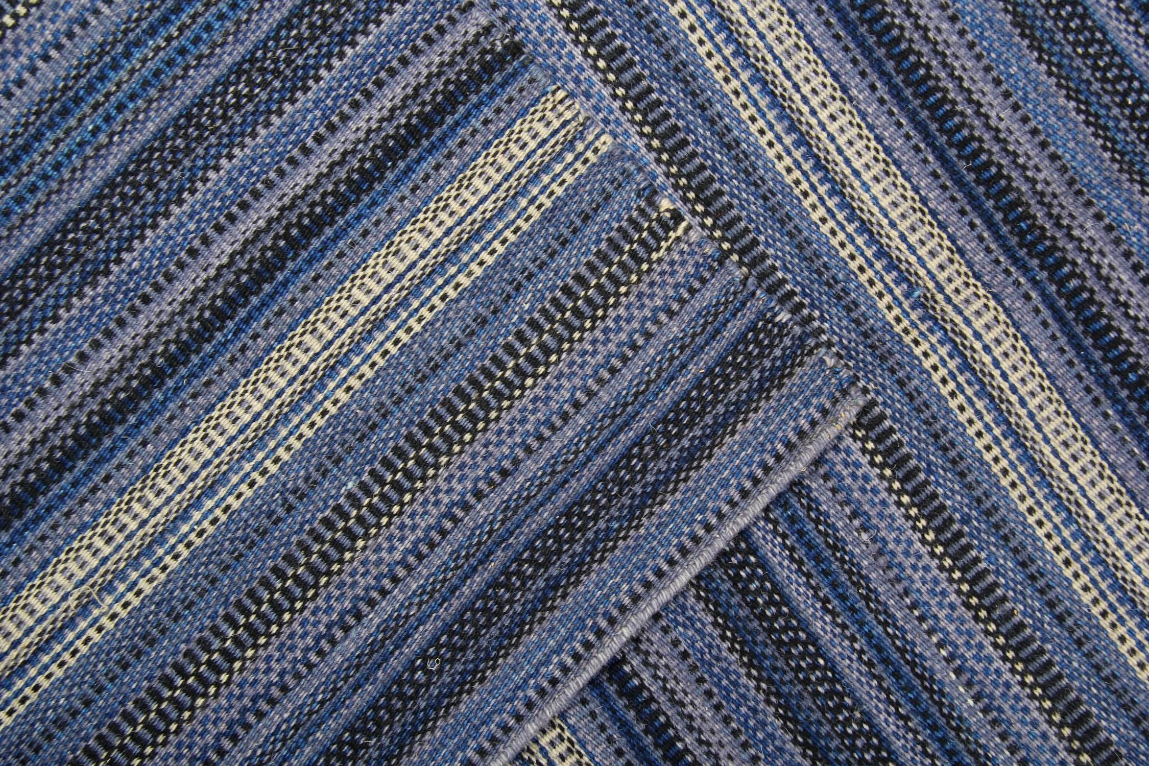 Ce fantastique tapis en laine est un Kilim tissé à la main, construit en Inde en 2000. Il présente un design à rayures simple mais accrocheur, avec des couleurs bleu blanc et gris. La couleur et le design de cette pièce en font le tapis parfait pour