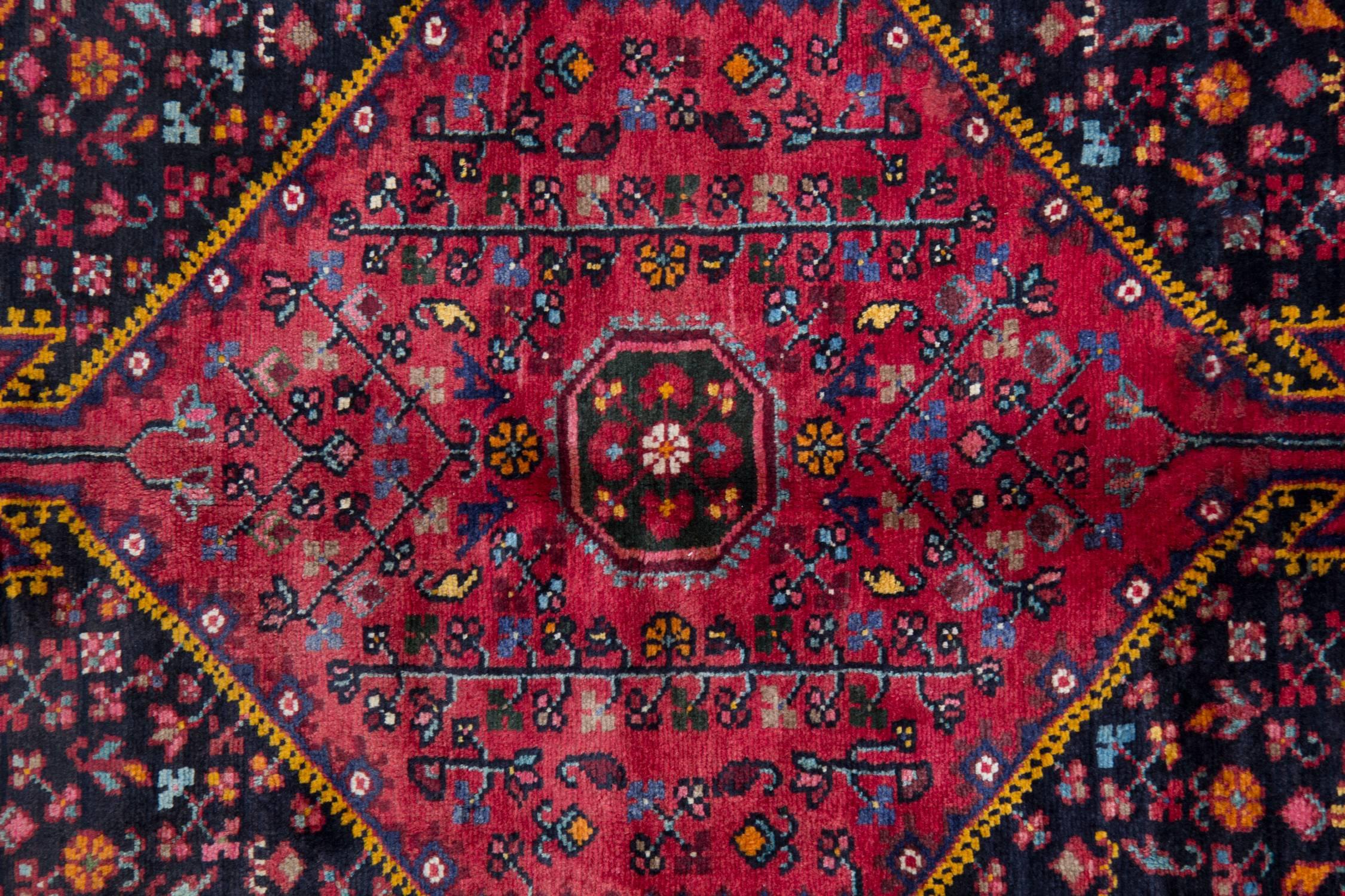 Ce tapis en laine d'un rouge profond a été tissé à la main avec des matériaux d'origine locale en Afghanistan dans les années 1970. Le motif présente un médaillon hexagonal avec des motifs et des dessins tissés de manière complexe, ainsi qu'un motif