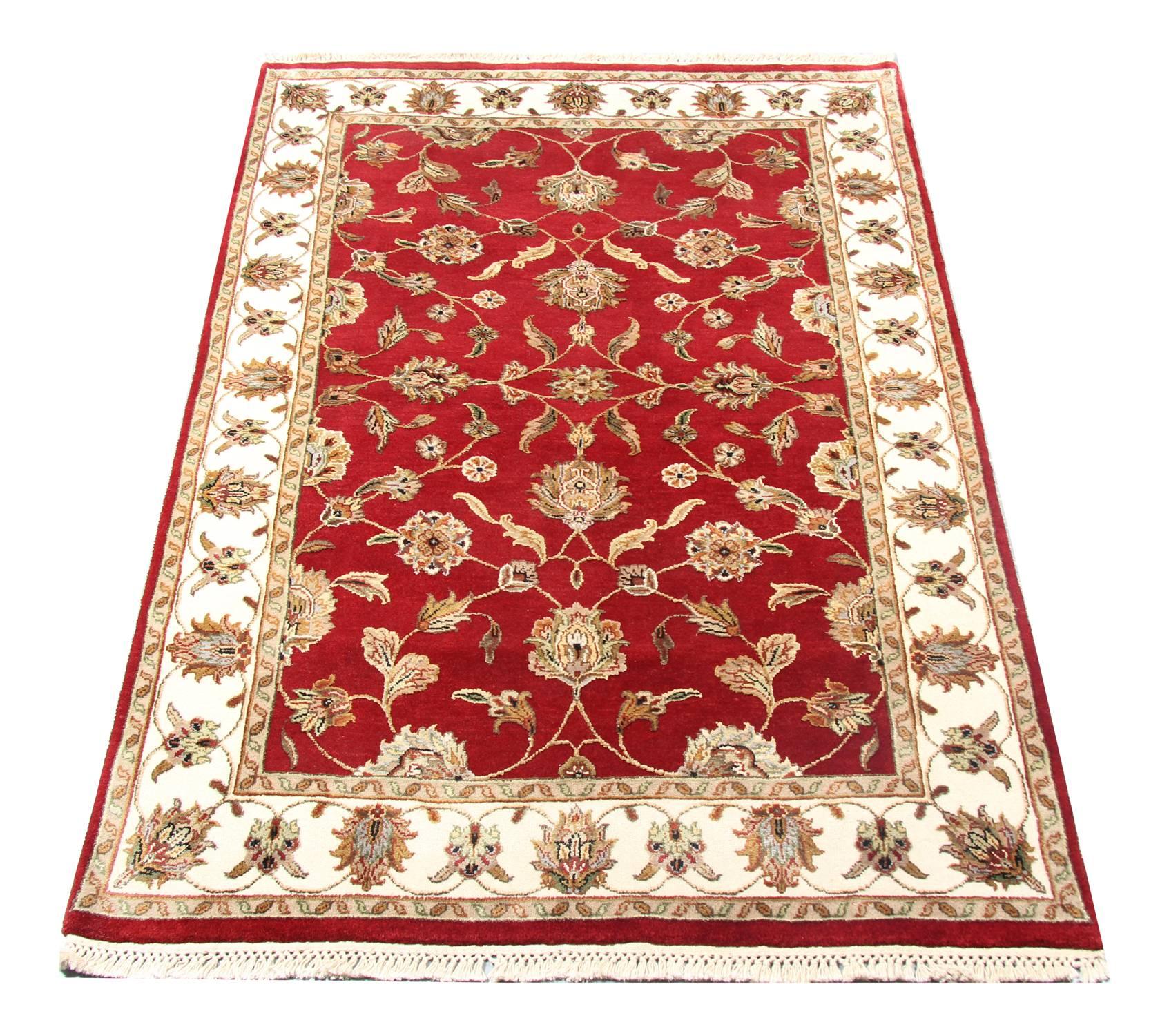 This elegant handmade wool rug was woven by master weavers on looms in Afghanistan. The central design features a rich red background with beige, cream and gold accent colors that make up the symmetrical, floral design. Intricately woven with