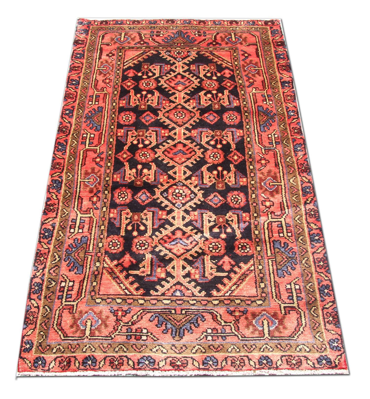 This elegant handmade wool rug was woven in Afghanistan in the mid 20th century with locally sourced materials. The central design features a fantastic tribal design woven on a deep blue background with red, cream and pink accents that make up the