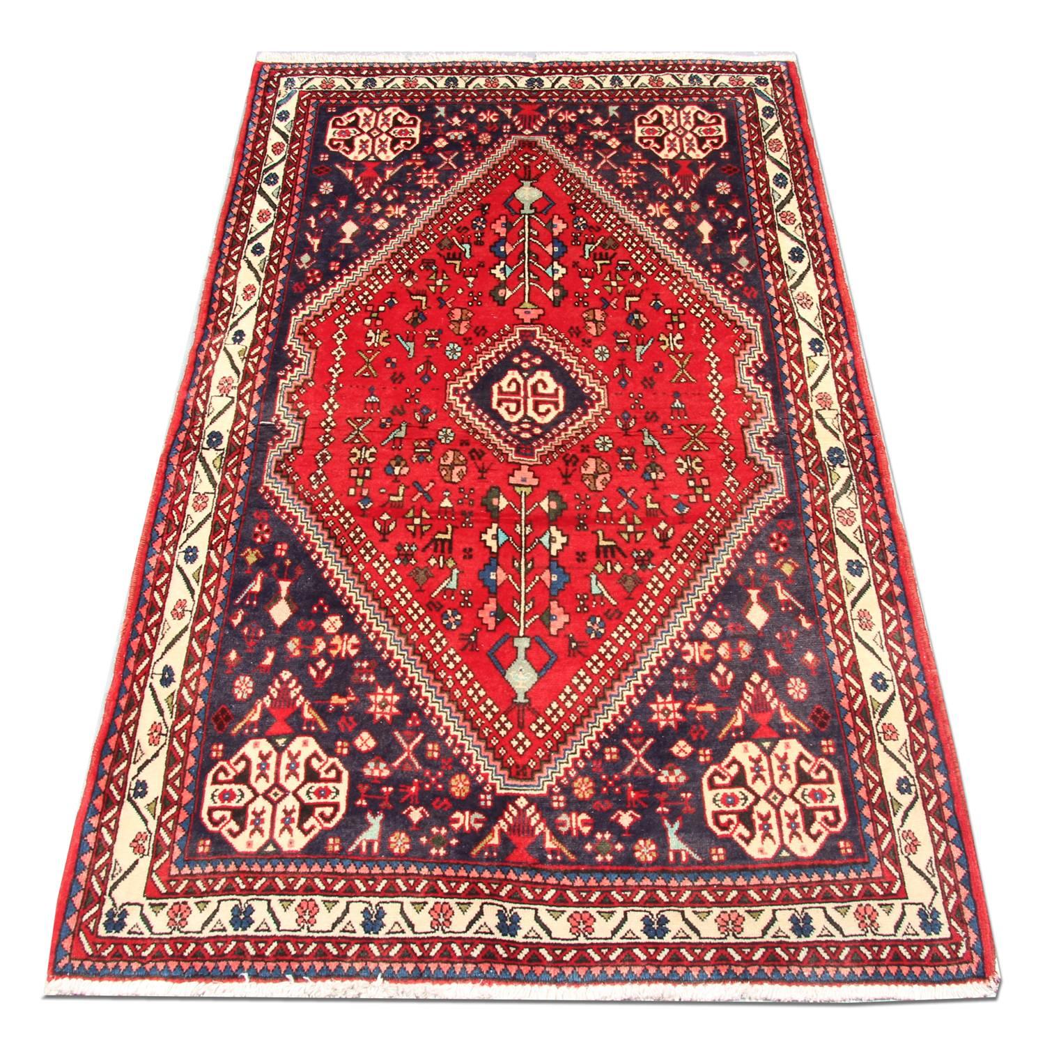 Dieser sattrote Wollteppich wurde im Iran aus feinster handgesponnener Wolle handgewebt. Das zentrale Design zeigt ein großes Medaillon mit einer dekorativen Umrandung und einer Bordüre, die in breiten blauen Akzenten gewebt ist, die einen eleganten