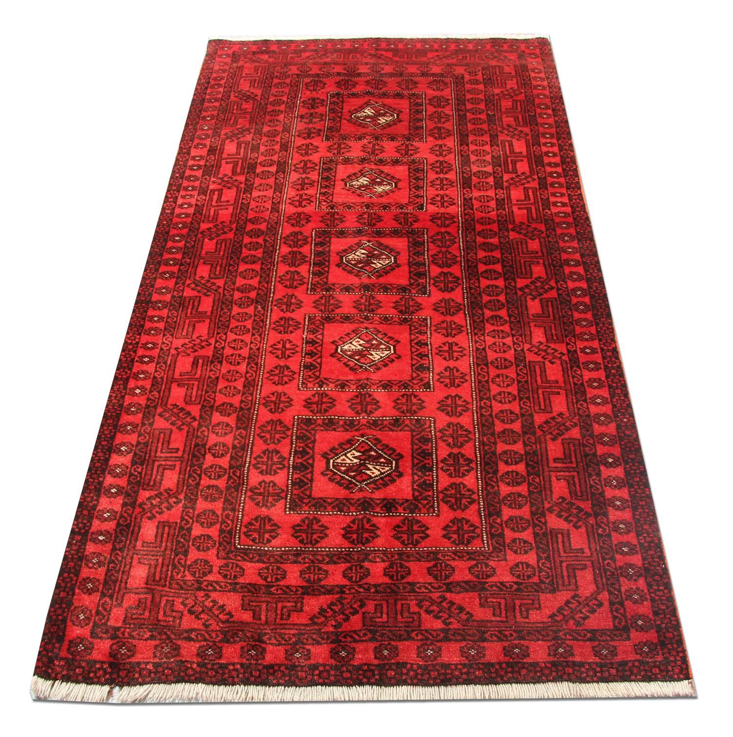 This rich red wool rug was handwoven in Afghanistan with the finest hand-spun wool. The central design features a repeat pattern medallion design with a decorative surround and border woven in broad blue accents that contrast elegantly with the