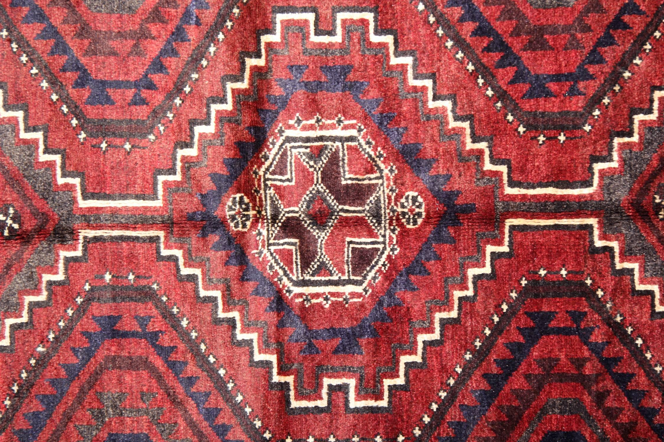 This elegant symmetrical oriental wool area rug was woven by hand in the 1970s. The design features a symmetrical tribal design woven on a rich red background with cream deep blue and brown accents. Featuring tribal motifs and medallions through