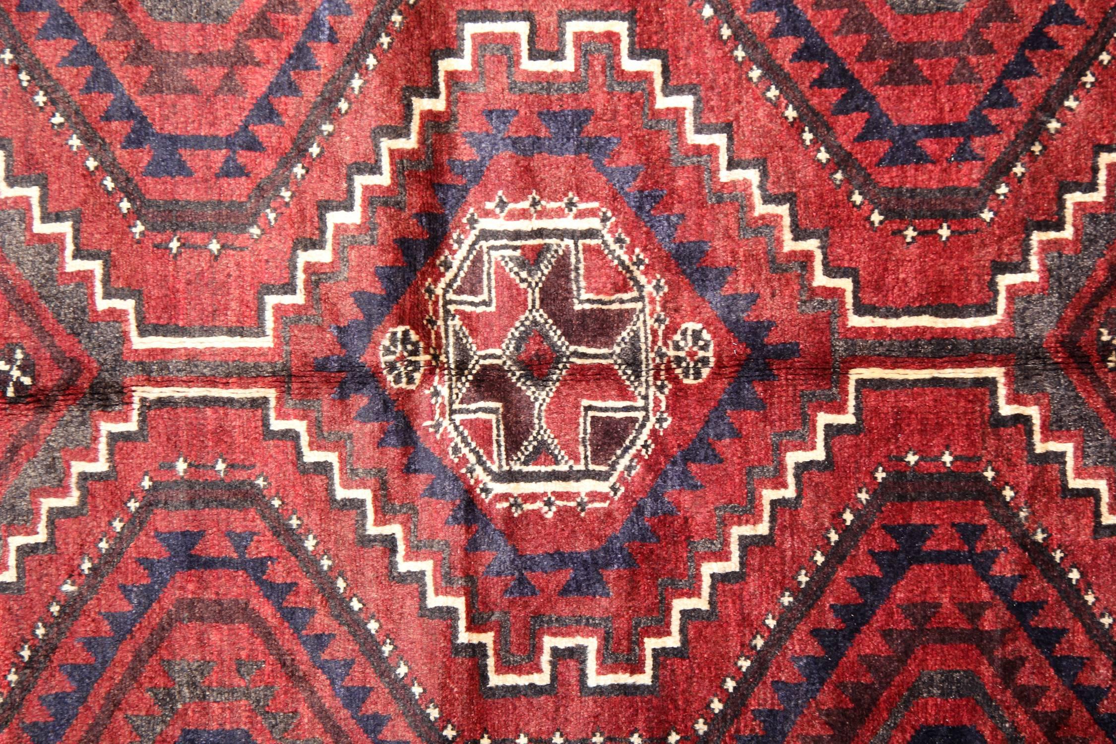 Esta elegante alfombra simétrica oriental de lana se tejió a mano en la década de 1970. Presenta un diseño tribal simétrico tejido sobre un rico fondo rojo con detalles en azul oscuro crema y marrón. Con motivos tribales y medallones tanto en el