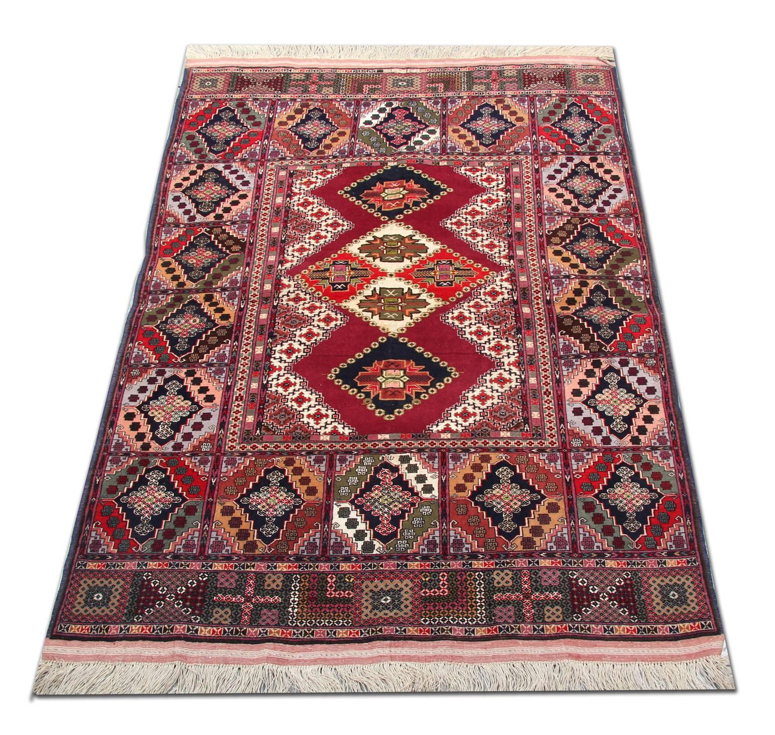 This geometric wool area rug was woven by hand with a fantastic tribal village design. The central pattern features a rich red background with diamond medallions which have been incorporated in accents of red, cream and deep blue. This is then