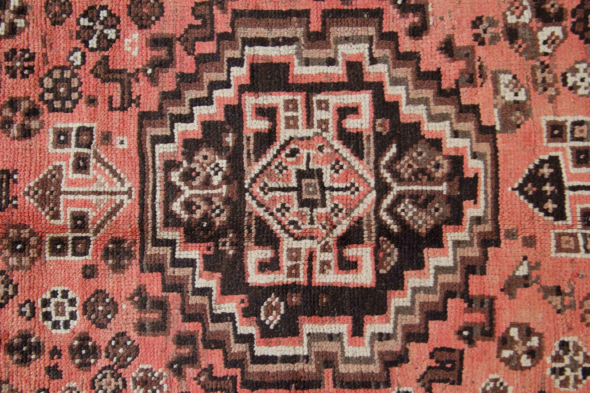 This fine wool area rug was woven with a fantastic orange-pink background. The central design features an intricate medallion and decorative motif surrounding design. This has then been framed by a brown symmetrical repeat pattern border that frames