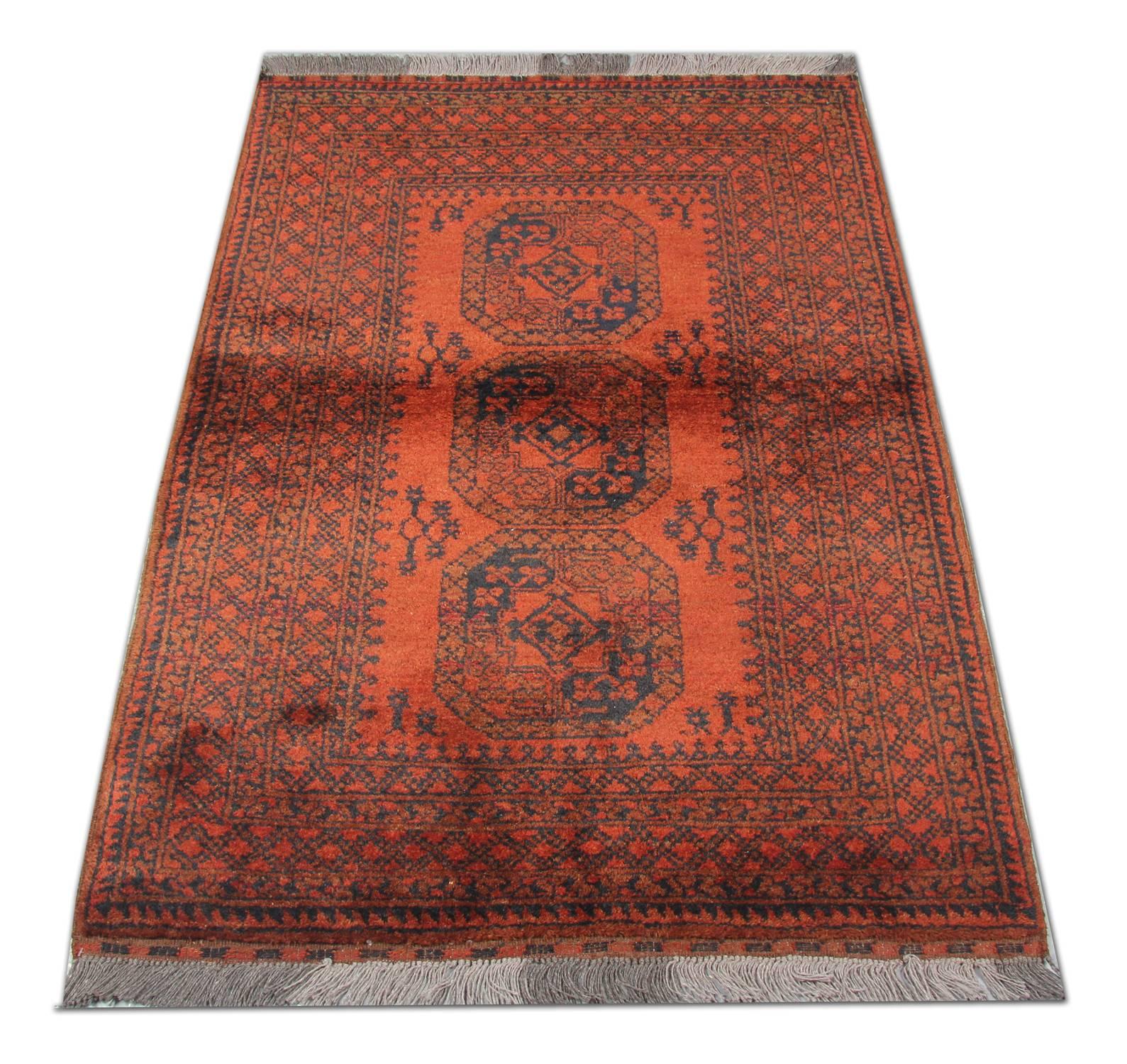 Ce tapis afghan traditionnel a été tissé à la main dans les années 1960. Le motif central présente trois grands médaillons, tissés en bleu profond sur un riche fond rouge. Le tout est ensuite agrémenté d'une bordure à motifs répétitifs très