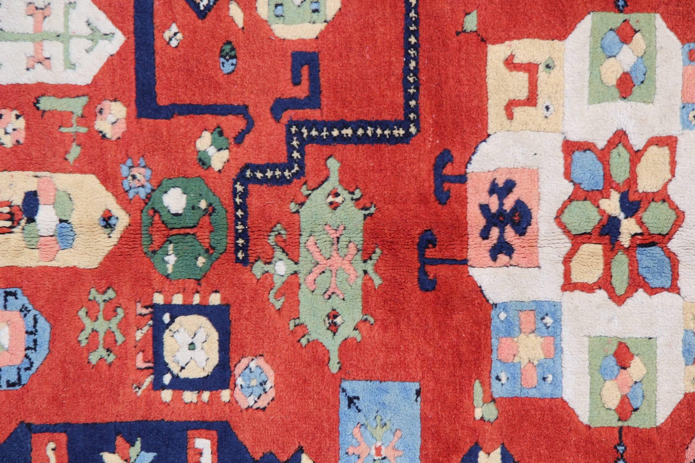 This truly unique wool rug features a top to bottom motif design. The red background is decorated with green, blue, cream and ivory accent motifs and medallions that float in an abstract design. The border is more regimented with a repeat pattern