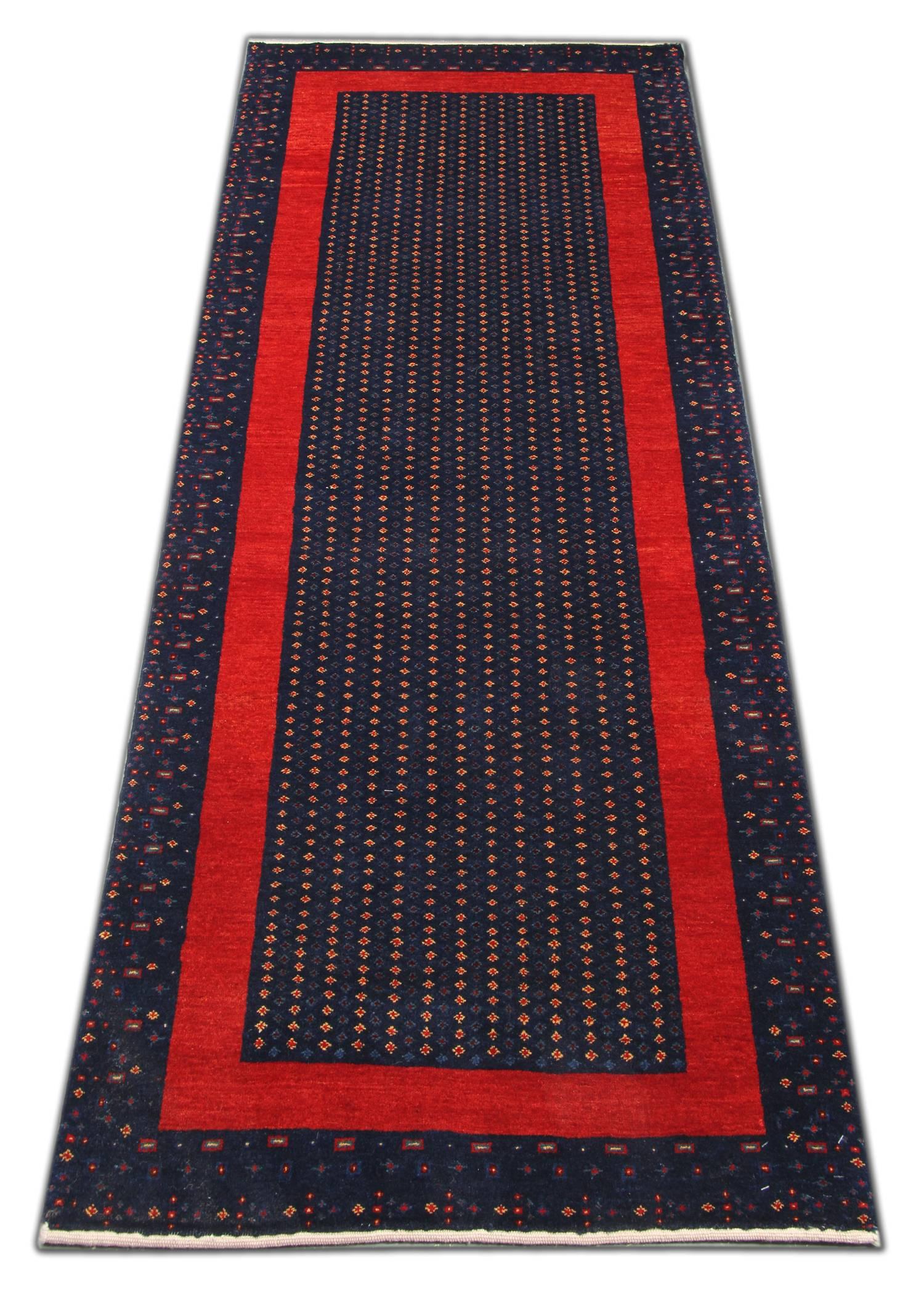 Dieser schlichte, handgewebte Wollteppich zeichnet sich durch einen tiefblauen Hintergrund mit einem einfachen, sich wiederholenden Muster aus gepunkteten Motiven und einer kräftigen, linearen Bordüre in kontrastierendem Rot aus. Dieser Teppich ist