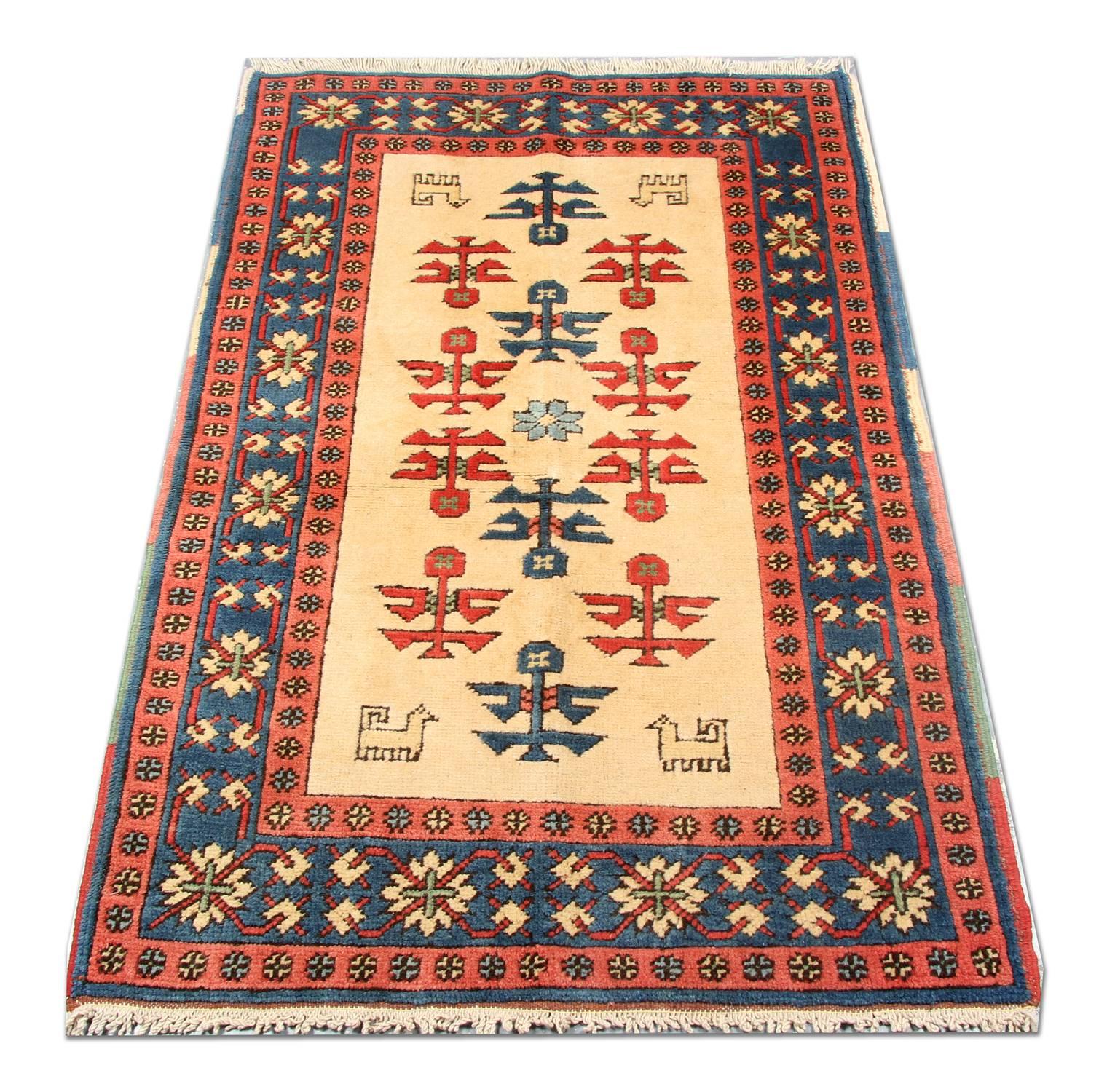 This tribal rug was woven by hand in the 1990s in Turkey with the finest wool materials. The central design features a cream field with a tribal motif design which has been symmetrically woven with red and blue accent colors and a layered repeat