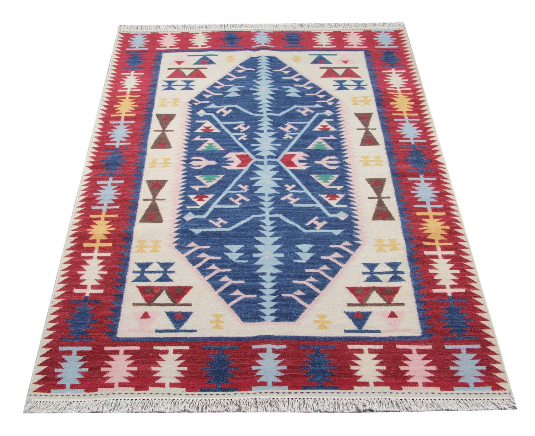 This handmade carpet blue rug is a flat-weave rug woven in stylish colours. On this tribal oriental rug, we can see light blue, dark blue, white, red and yellow colours. The geometric rug has an elegant red border with same shaped patterns in