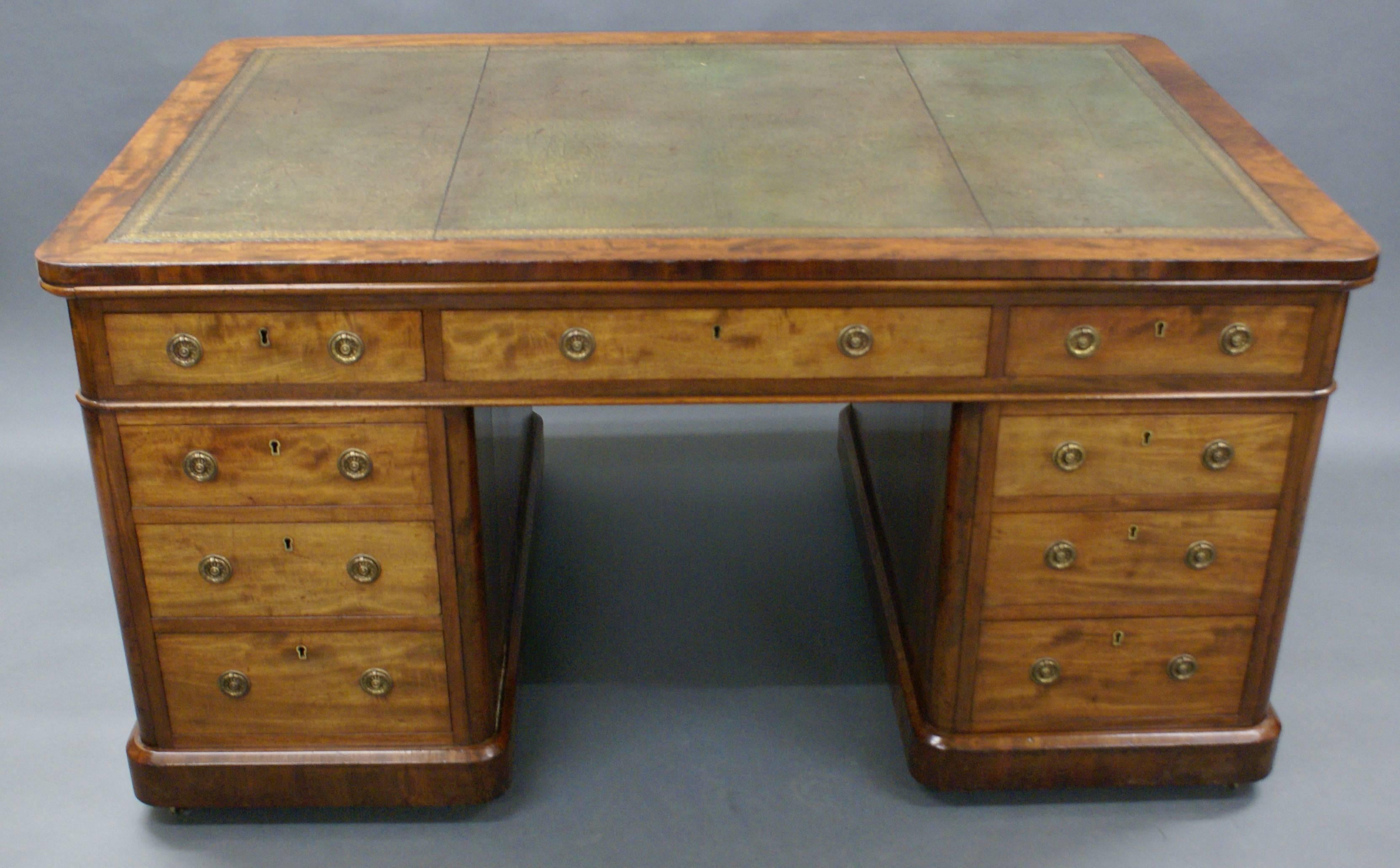 In well figured mahogany with nine mahogany lined drawers to one side and three drawers over two cupboards on the reverse. With re-entrant corners and standing on castors, this lovely desk has a long grain banding surrounding a gilt tooled leather