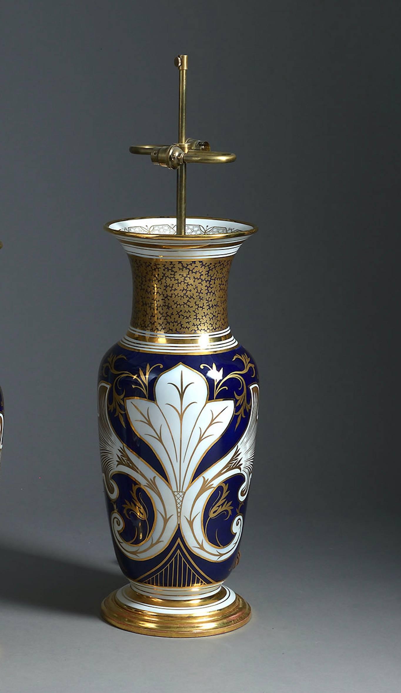 An exceptional pair of large scale Paris porcelain vases decorated with floral panels on one side and a stylised floral motif to the other side. Each body with gilded seaweed decoration to the neck and a dark blue ground. Now mounted as lamps gilded