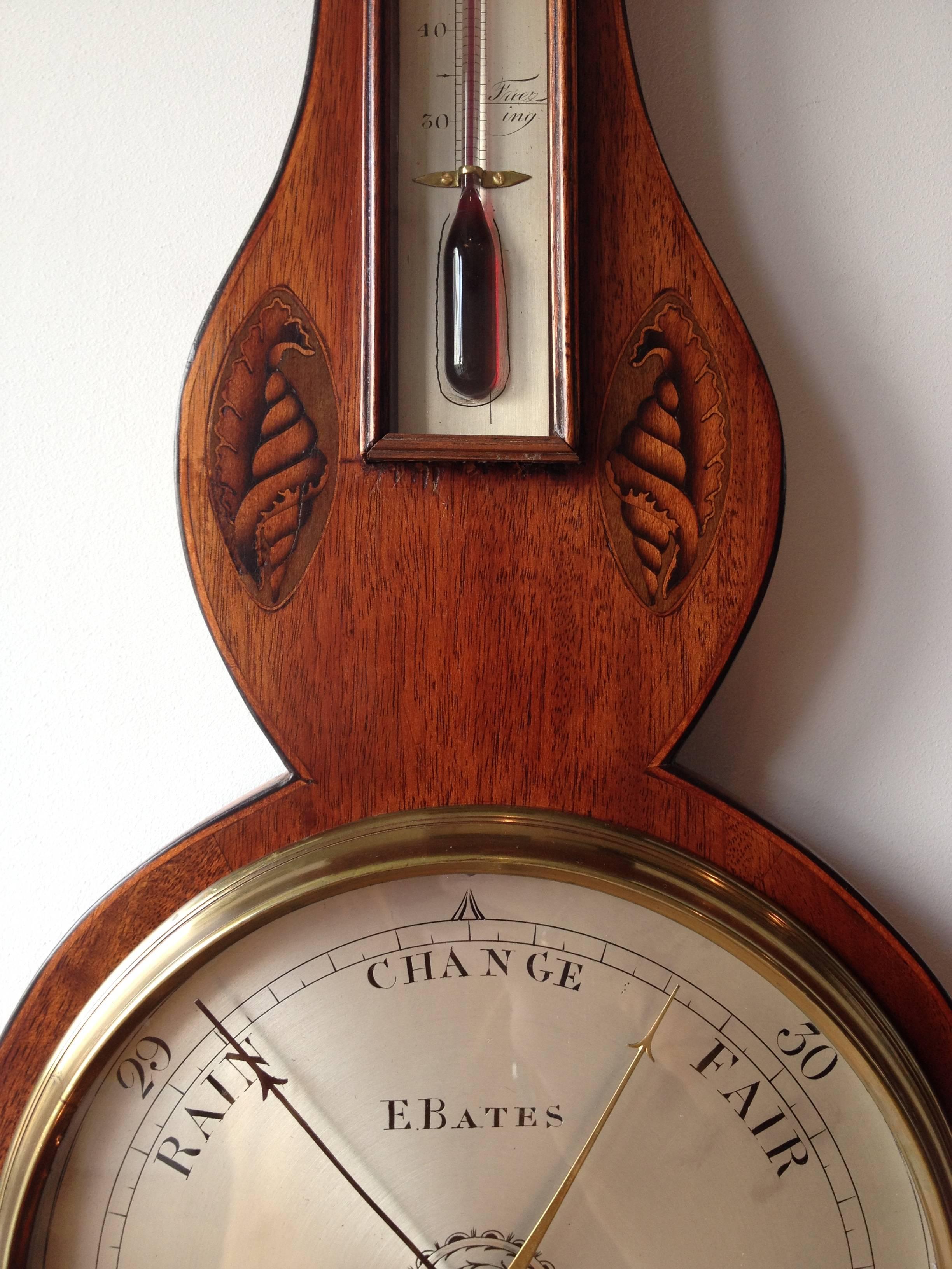 A late Georgian mahogany wheel barometer with satinwood marquetry inlay by Bates of Kettering. 

The mahogany case has satinwood stringing and marquetry shell and sunflower inlay decoration and is crowned by an architectural pediment with central