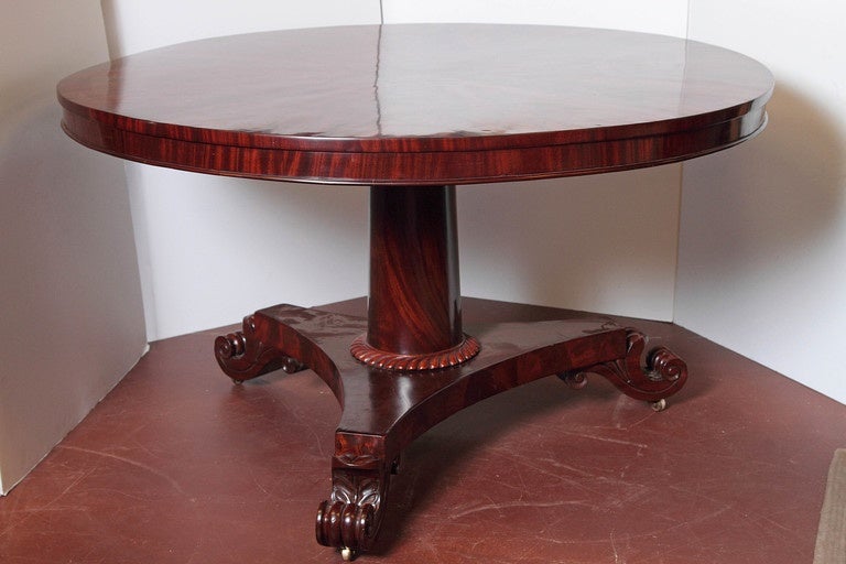 William IV round center table with bookmatched crotch-grain mahogany, raised on column with tripartite base ending in scroll feet with castors, England.