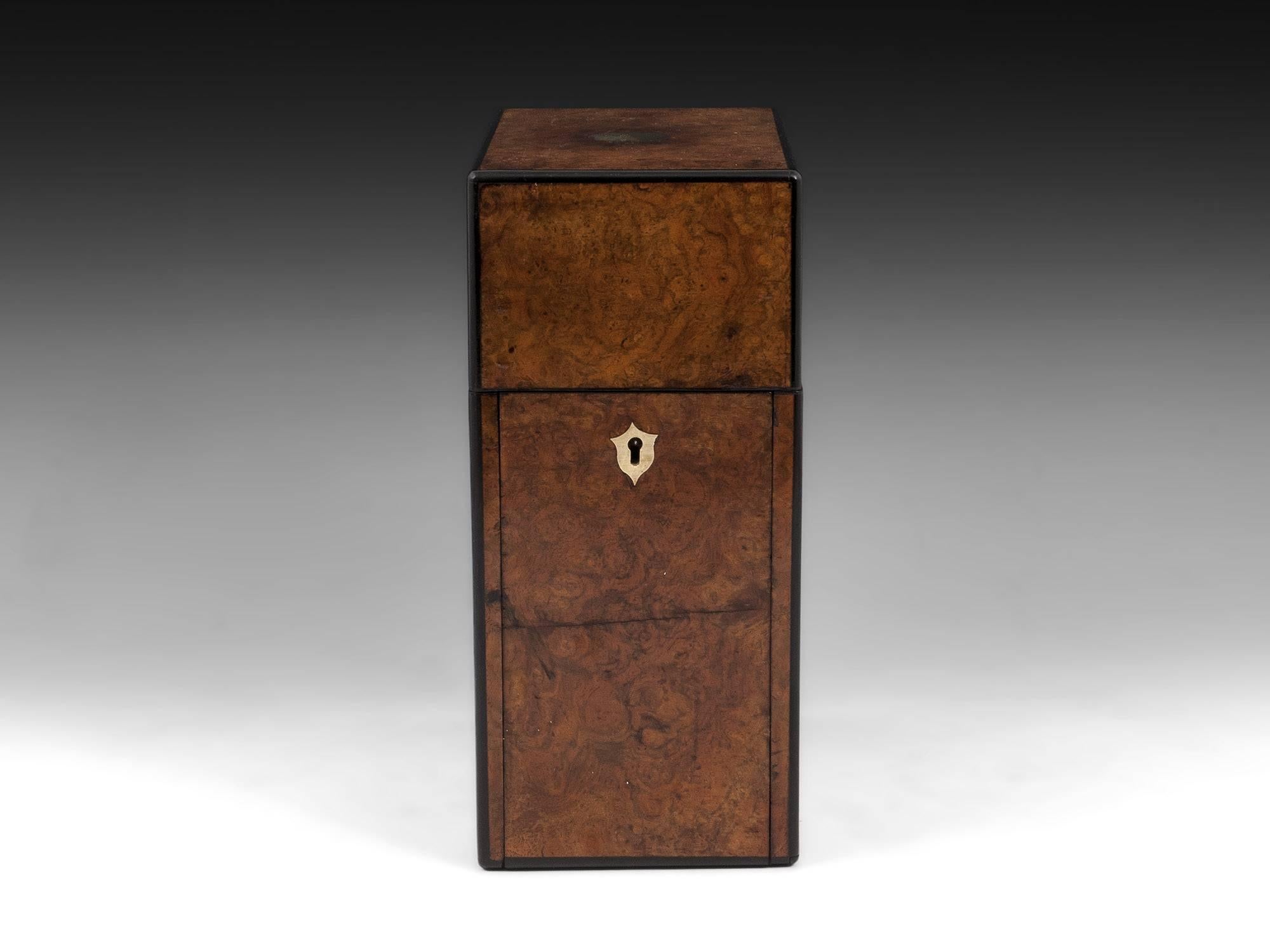Antique burr walnut decanter box with ebony edging, vacant brass initial plate and brass escutcheon. 

Lifting the lid of the single decanter box allows the front of the box to fall forward revealing a single glass decanter with pouring spout and