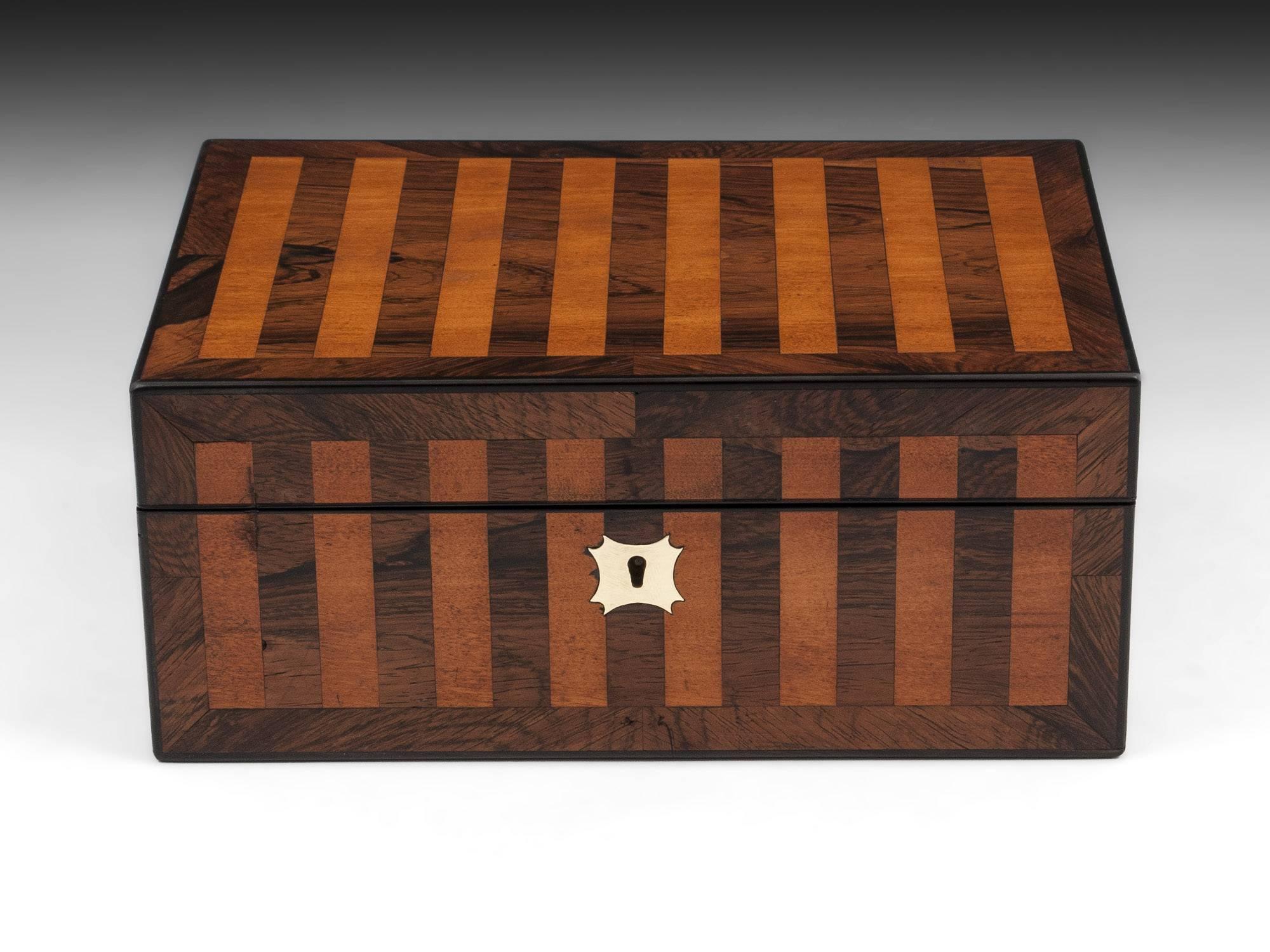 Antique jewelry box with inlaid mahogany and satinwood stripes to the front and top with an ornate brass escutcheon. 

Opening the box reveals the striking royal blue velvet and silk paper lined interior, which features a removable jewelry tray