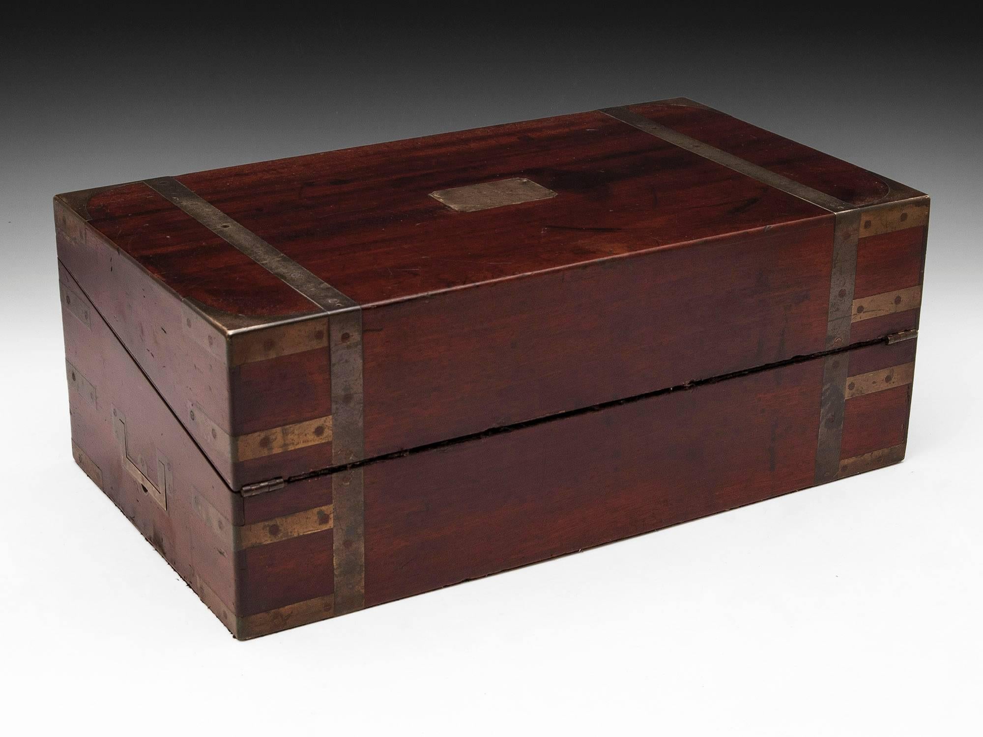 Georgian military mahogany writing box with brass straps running from front to back, brass corner braces, initial plate and ornate escutcheon. Contains secret drawers and has fantastic patination. 

The interior features its original baize cloth