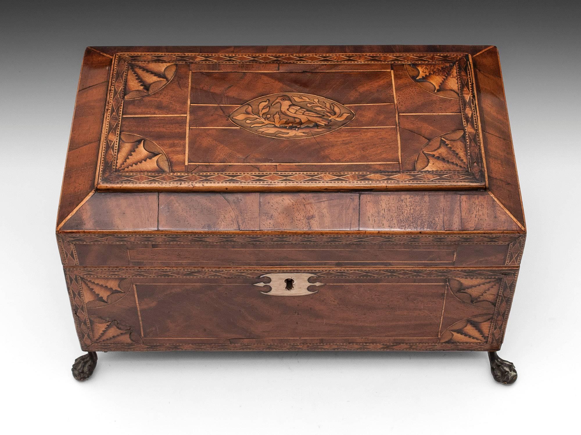 Flame Mahogany Tea Chest with beautiful patination, diamond shaped banding and quarter fan inlays. Standing on four brass ball and claw feet. The top is inlaid with a naive bird perched on a branch. 

The interior features the original quartered