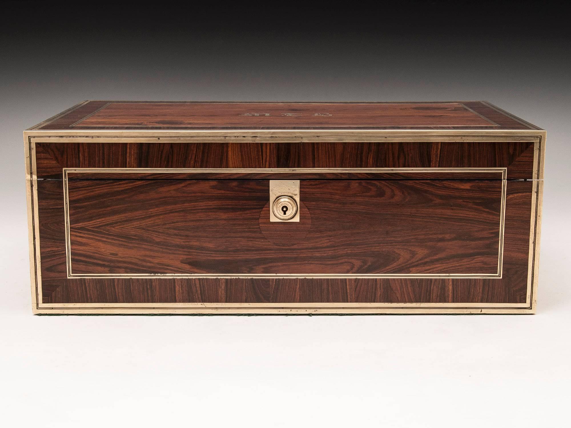 Kingwood writing box with brass stringing, escutcheon, carrying handles and a secret compartment containing two drawers. 

The interior features its original navy blue and gold tooled writing surface, two brass screw top ink wells and a removable
