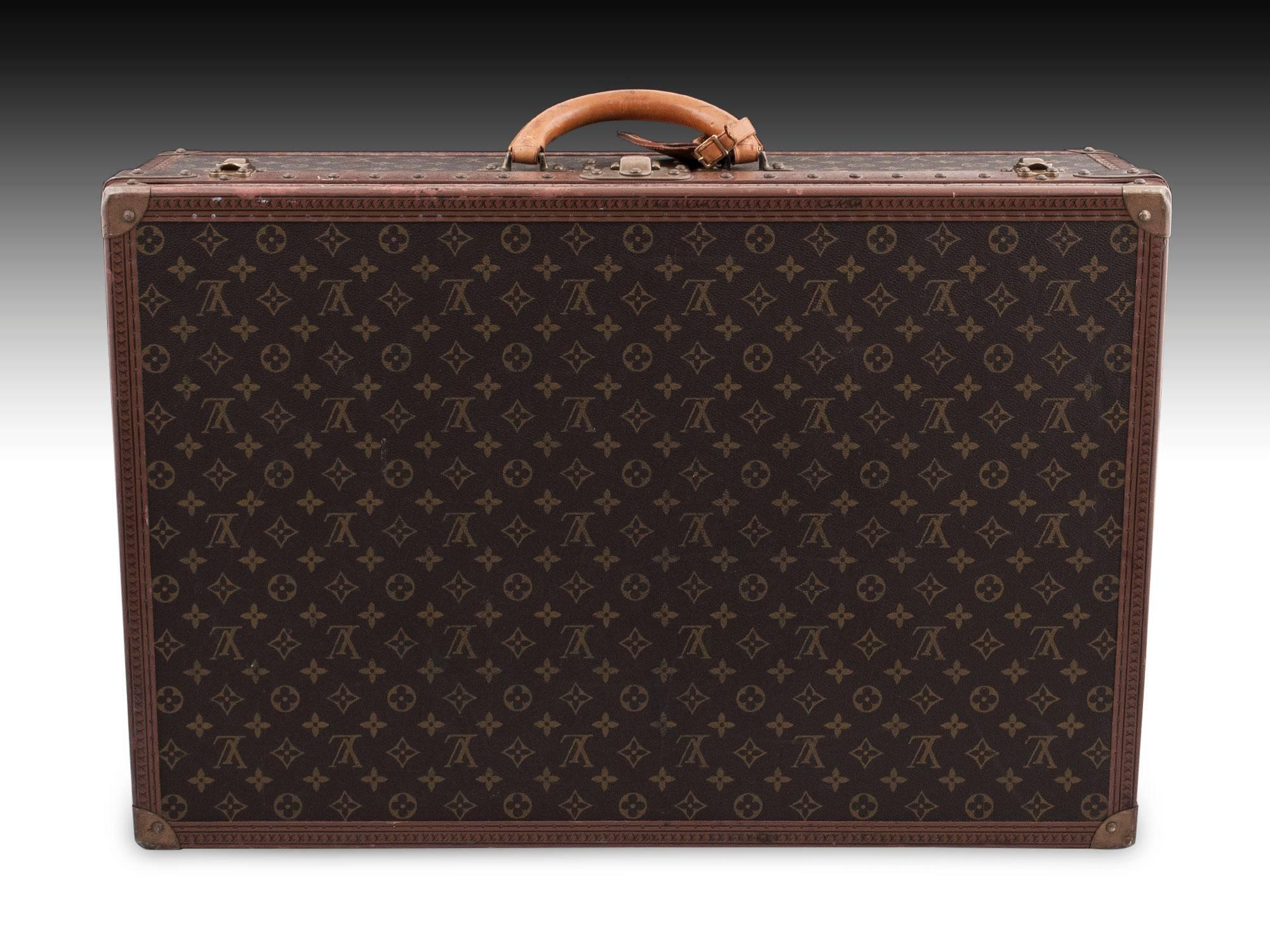 Louis Vuitton luxury hard-sided vintage suitcase with monogram canvas, riveted edging, brass corner brackets lock and latches. With a rounded leather handle with original Louis Vuitton leather tag. 

The interior features two straps with Louis