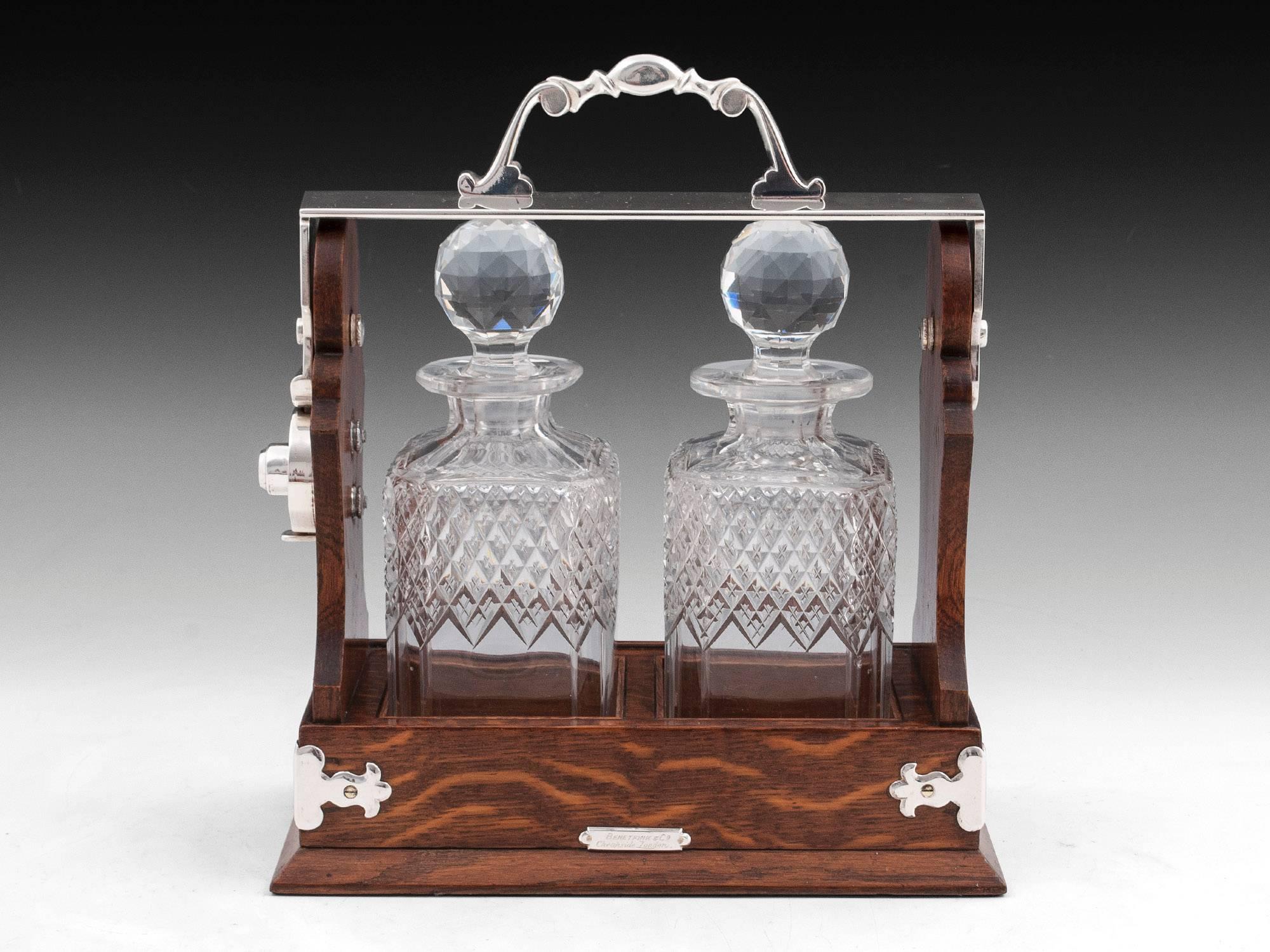 Two bottle Betjemann oak tantalus with silver plated swing carry handle with matching decorative corner supports. The lead crystal decanters feature beautiful half diamond cut body with star cut bases and faceted stoppers.

On the plinth base is a