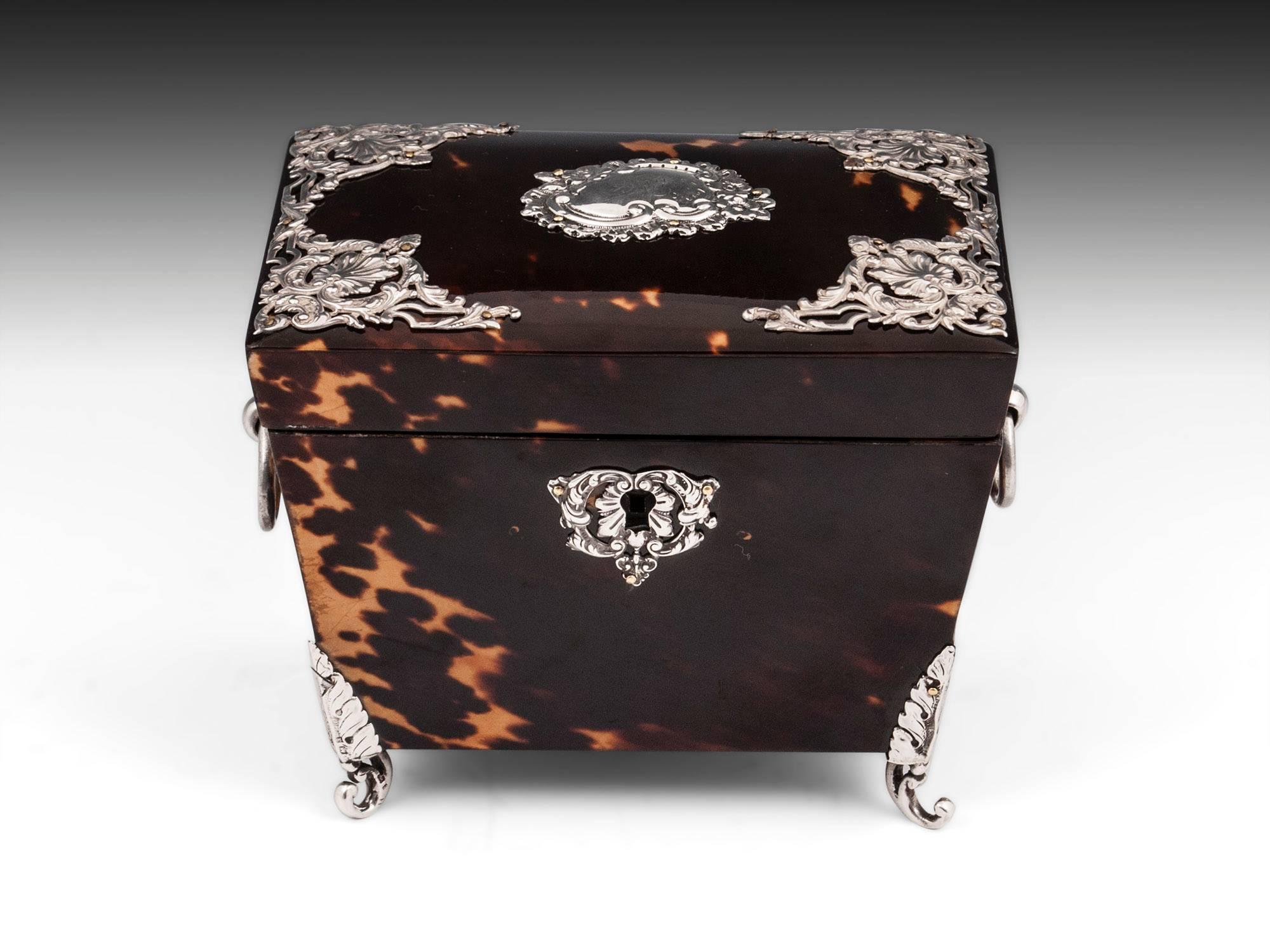 Tortoiseshell and silver tea caddy with pressed and pierced silver decorations, ornate engraved initial plate, escutcheon and has solid silver ring handles and stands on ornate elegant feet. 

The interior of the tortoiseshell & silver tea caddy