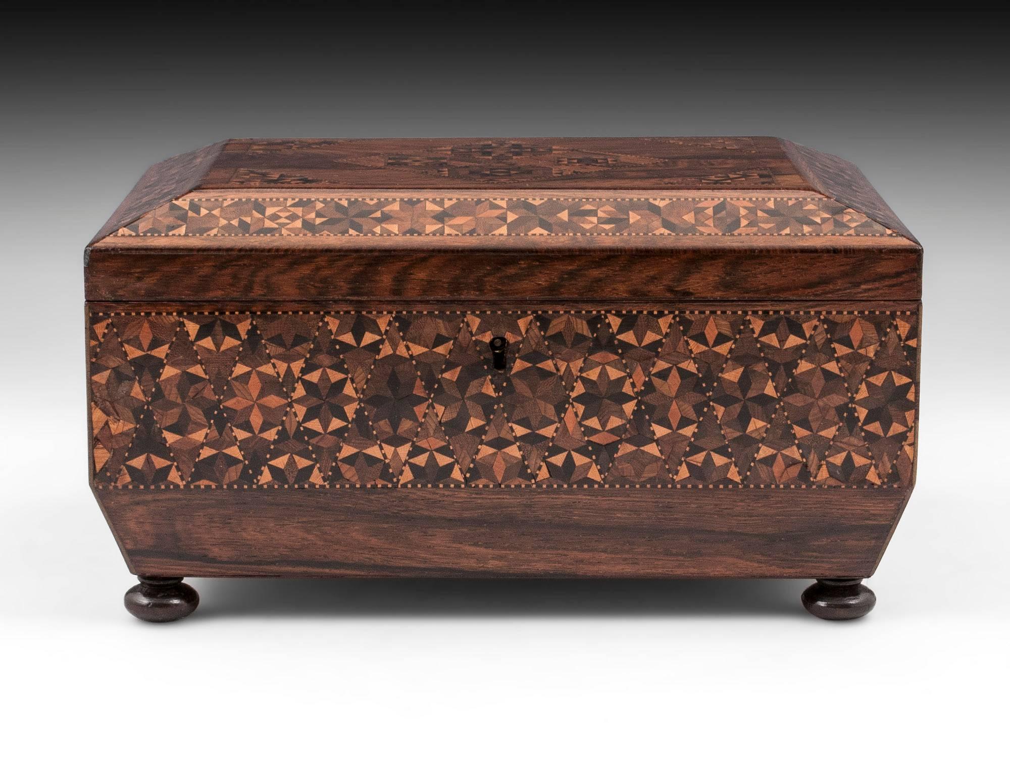 Tunbridge ware sewing box veneered in mahogany with micro mosaic bands running around the box with triangle and diamond patterns on the top. 

The Tunbridge sewing box interior features a removable yellow paper lined tray that contains six thread