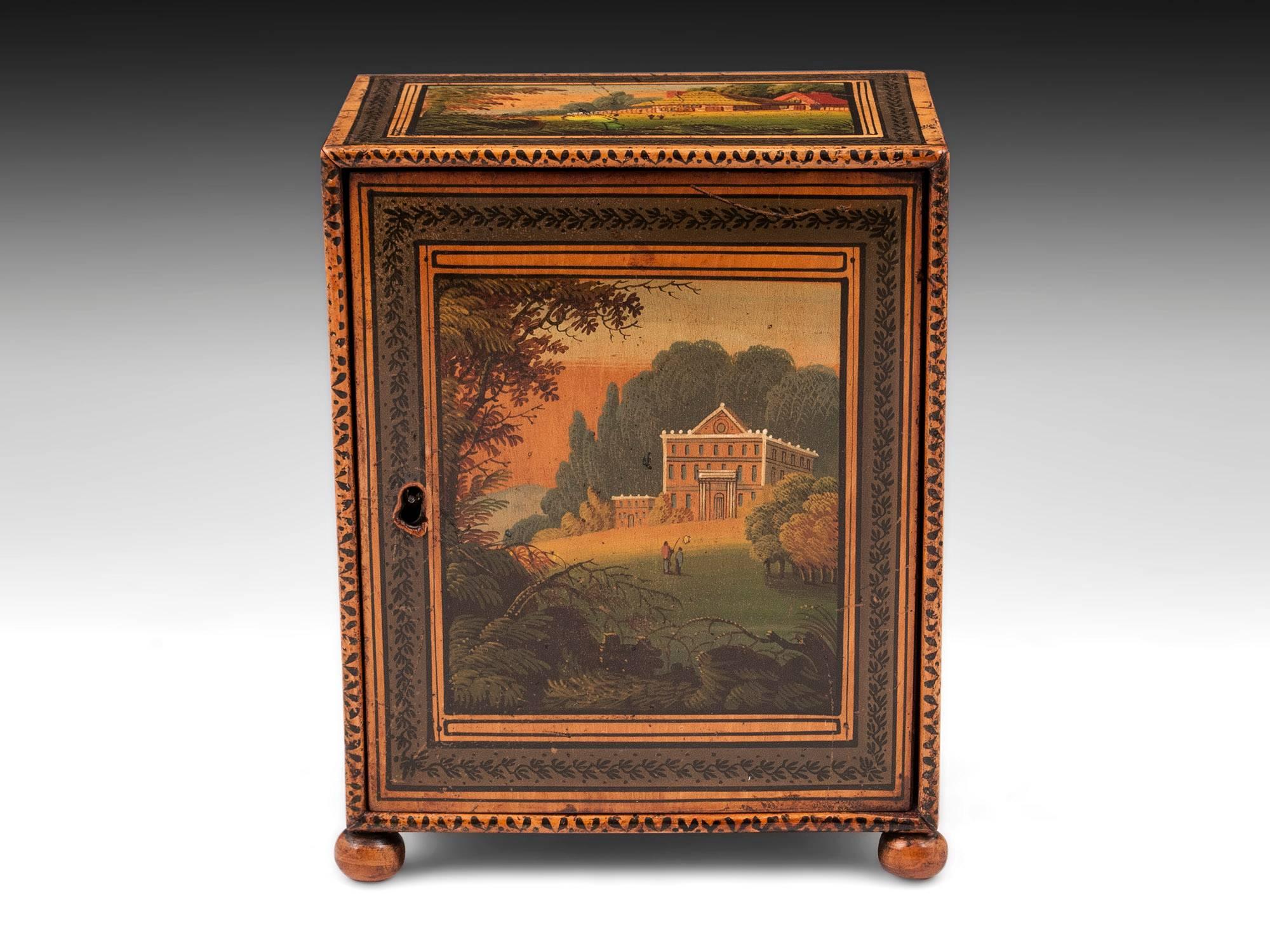A charming early Tunbridge ware sewing cabinet with finely detailed painted landscape scenes to the front, sides and top. Stands on four turned wooden bun feet. The door opens to reveal three drawers, each paper-lined and with a turned bone handle.