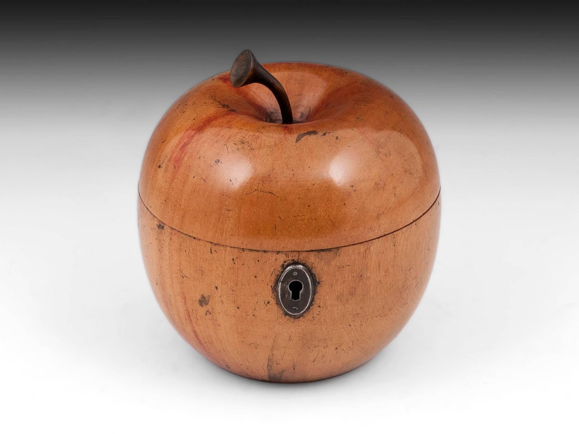 Apple tea caddy with wonderful red blushing to the exterior and realistic stalk. The apple tea caddy has a oval cut steel escutcheon. 

This treen apple tea caddy still has traces of tin lining, comes with a fully working lock and tasselled key,