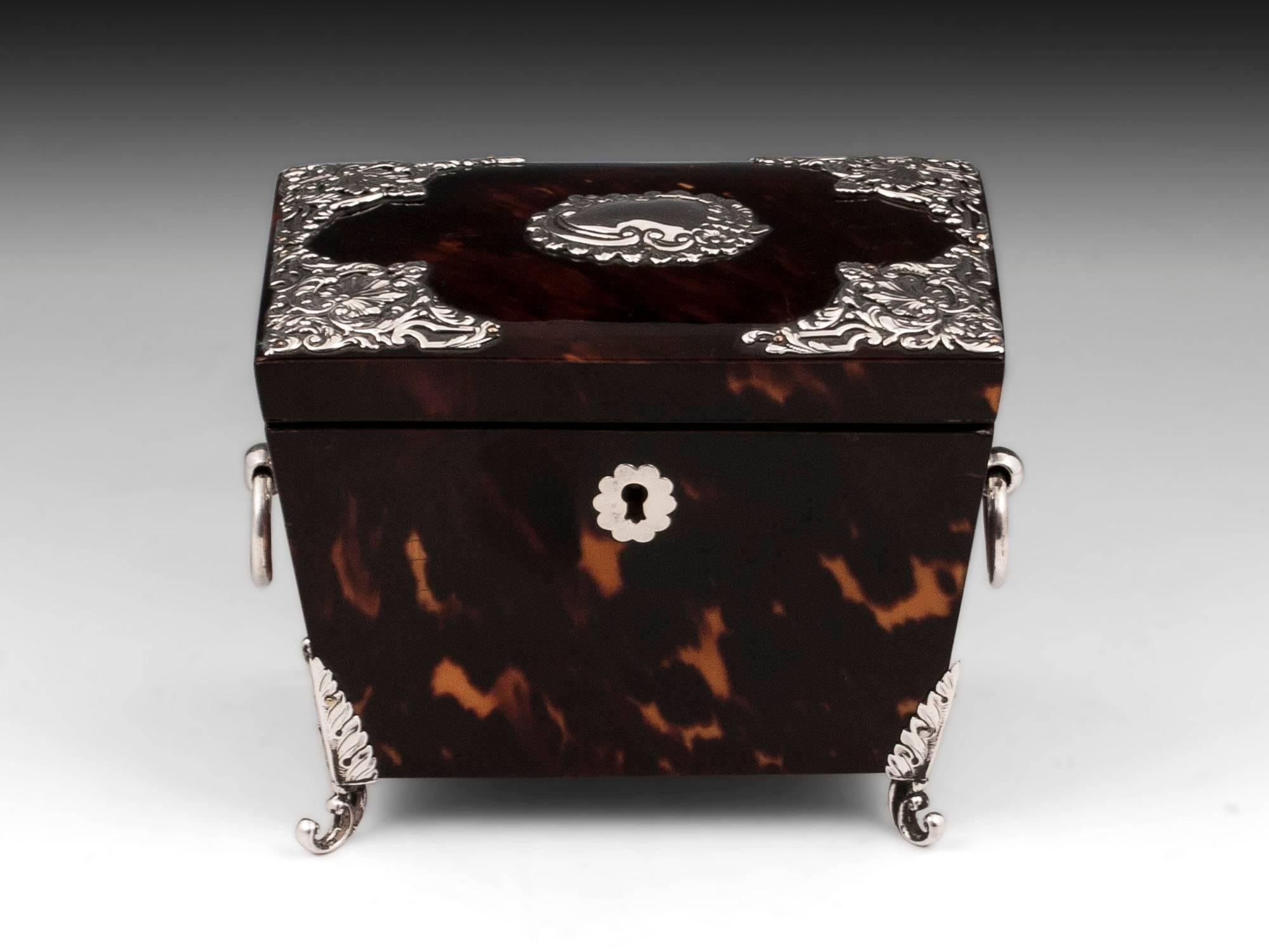 Tortoiseshell and silver tea caddy with pressed and pierced silver mounts, ornate engraved initial plate, escutcheon and has solid silver ring handles and stands on ornate scrolling elegant feet. 

The interior of this delightful tortoiseshell and
