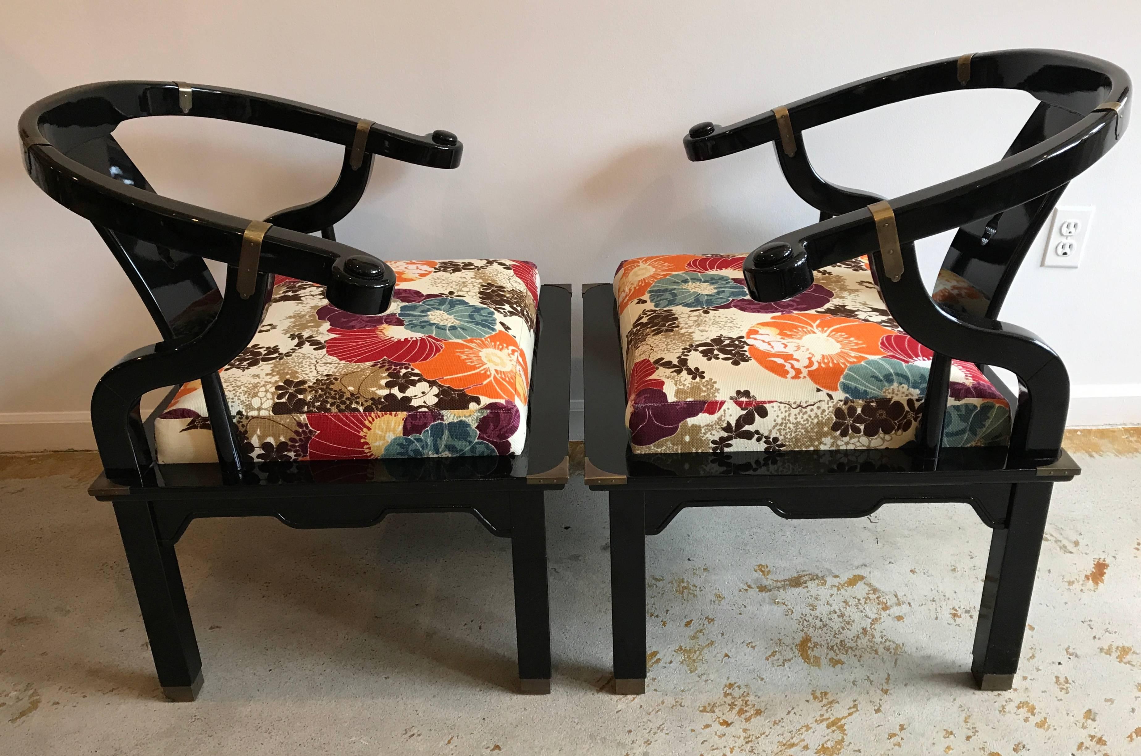Beautiful pair of Asian black lacquer club chairs with patina brass accents. Similar to James Mont Chinese horseshoe back chairs.  Very good condition. Very sturdy. Great medium size for any size space. Reupholstered in vibrant floral fabric.